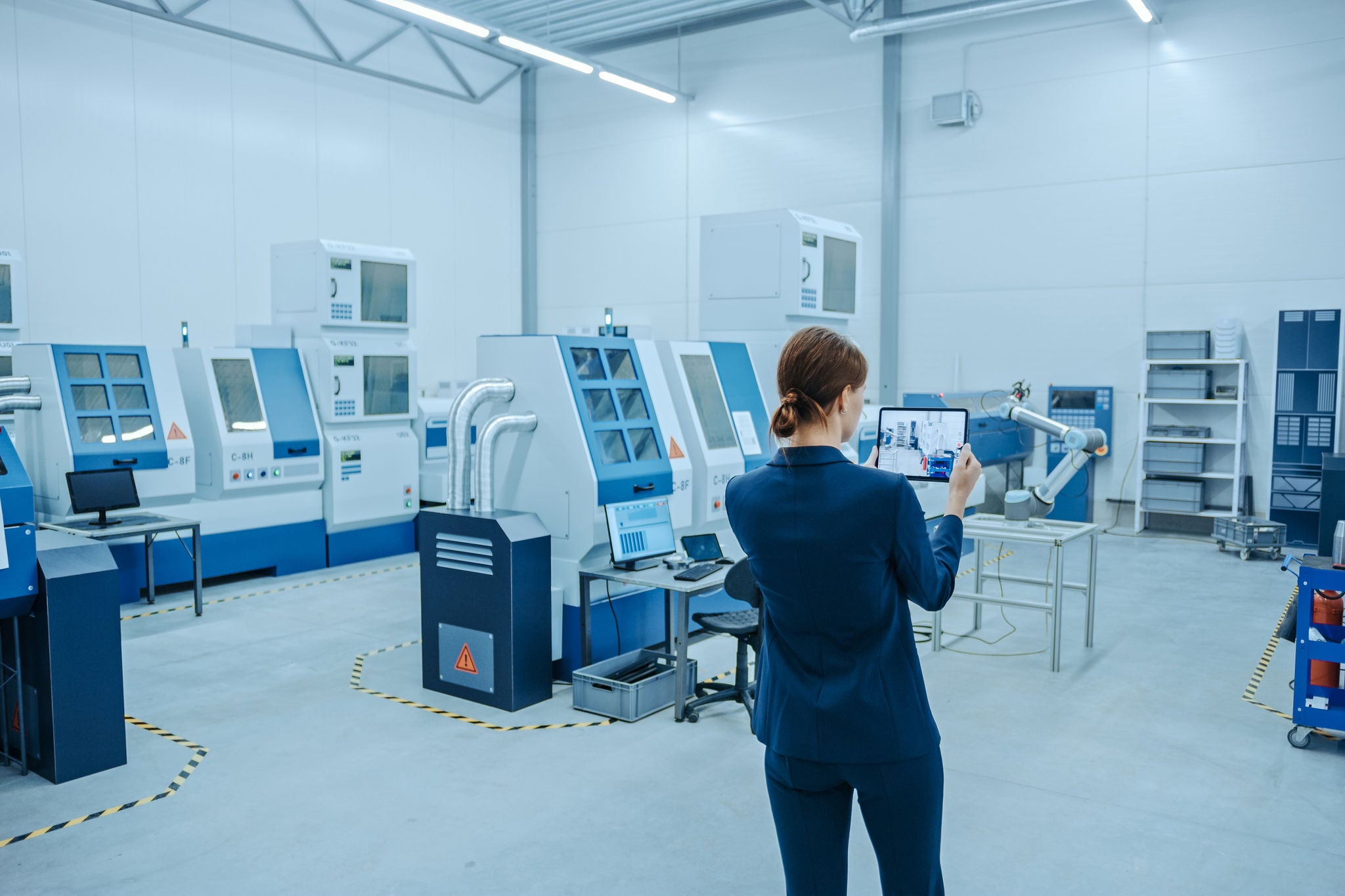 Modern Factory: Female Engineer Uses Digital Tablet Computer with Augmented Reality Software to Visualize Workshop for Room Mapping, Floor Layout. Facility with High-Tech CNC Machinery and Robot Arm