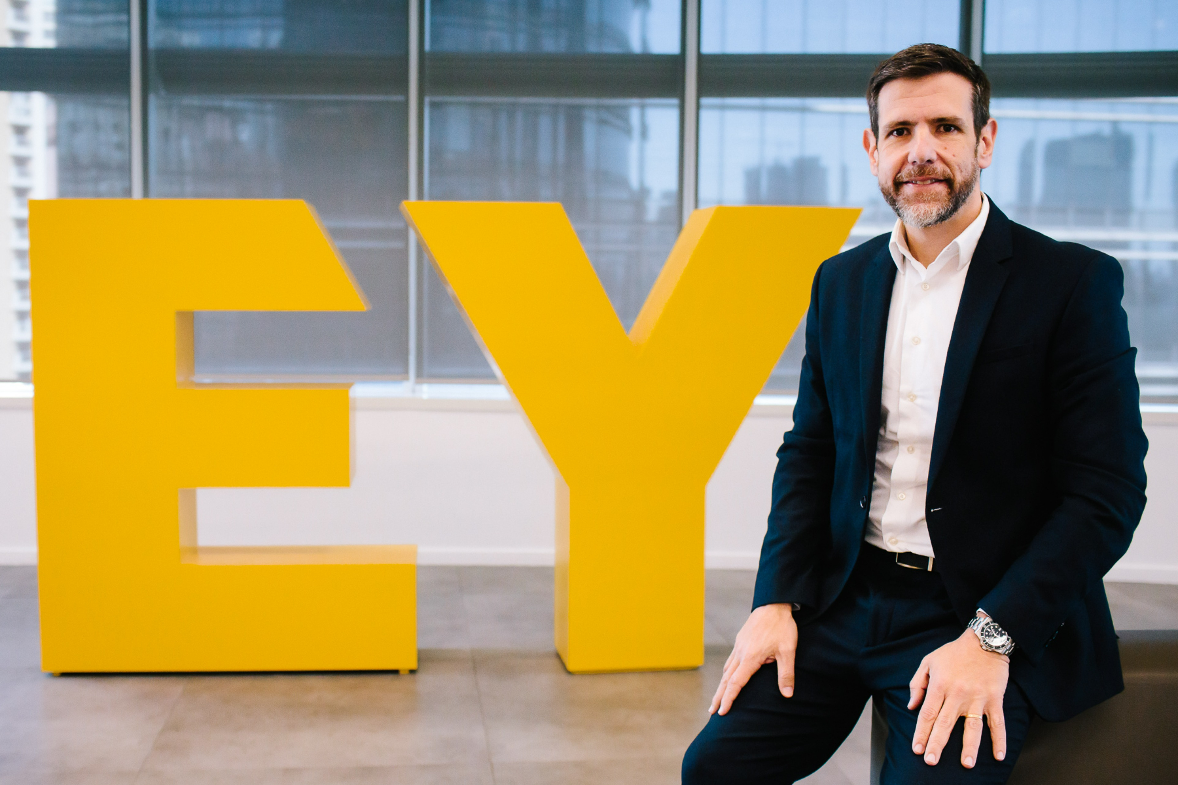 Ricardo Assumpção em fotografia ao lado do Logo da EY