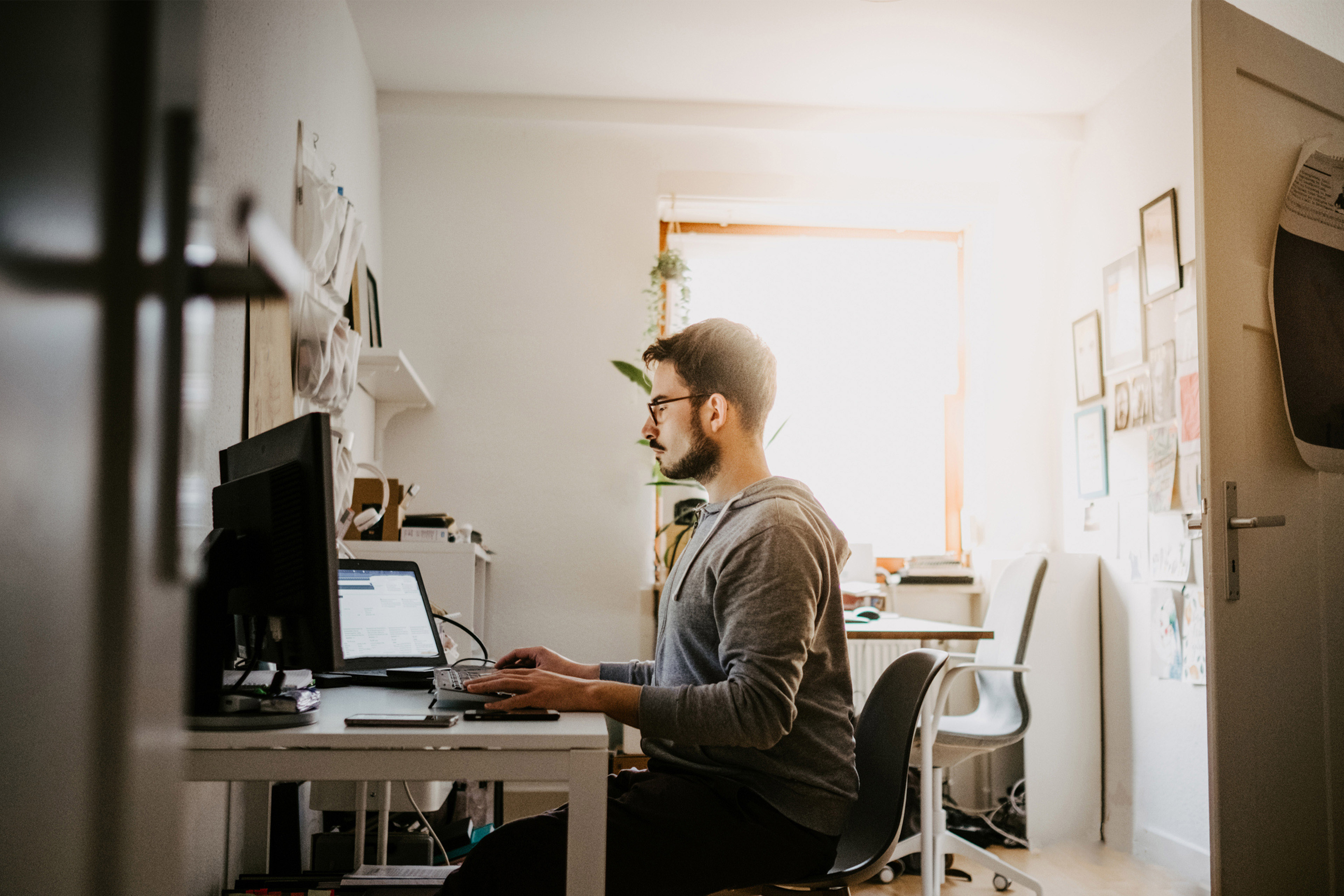 Mann arbeitet von zu Hause aus an Laptop und Desktop