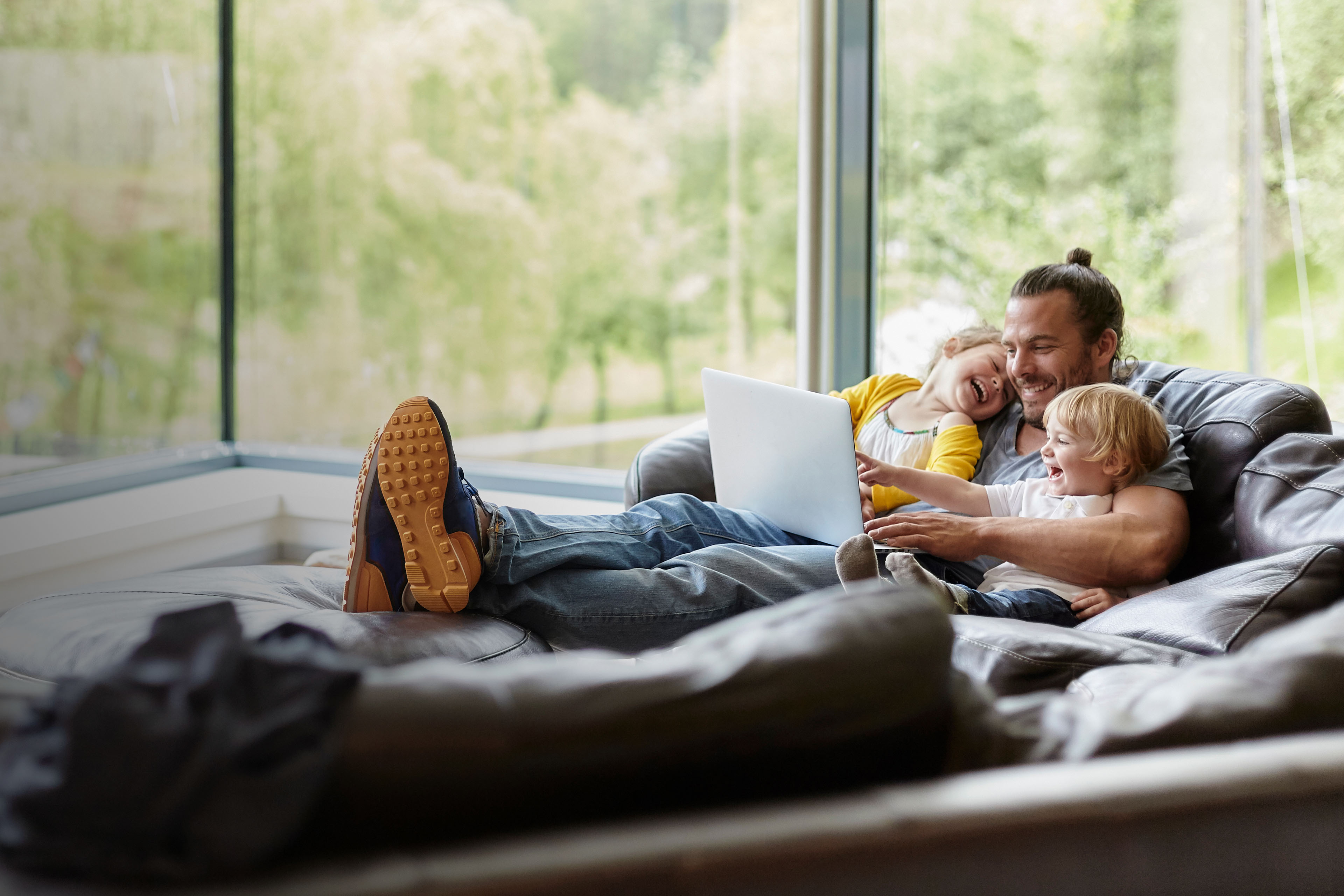 Vater und zwei kinder liegen auf der couch und schauen auf einen laptop