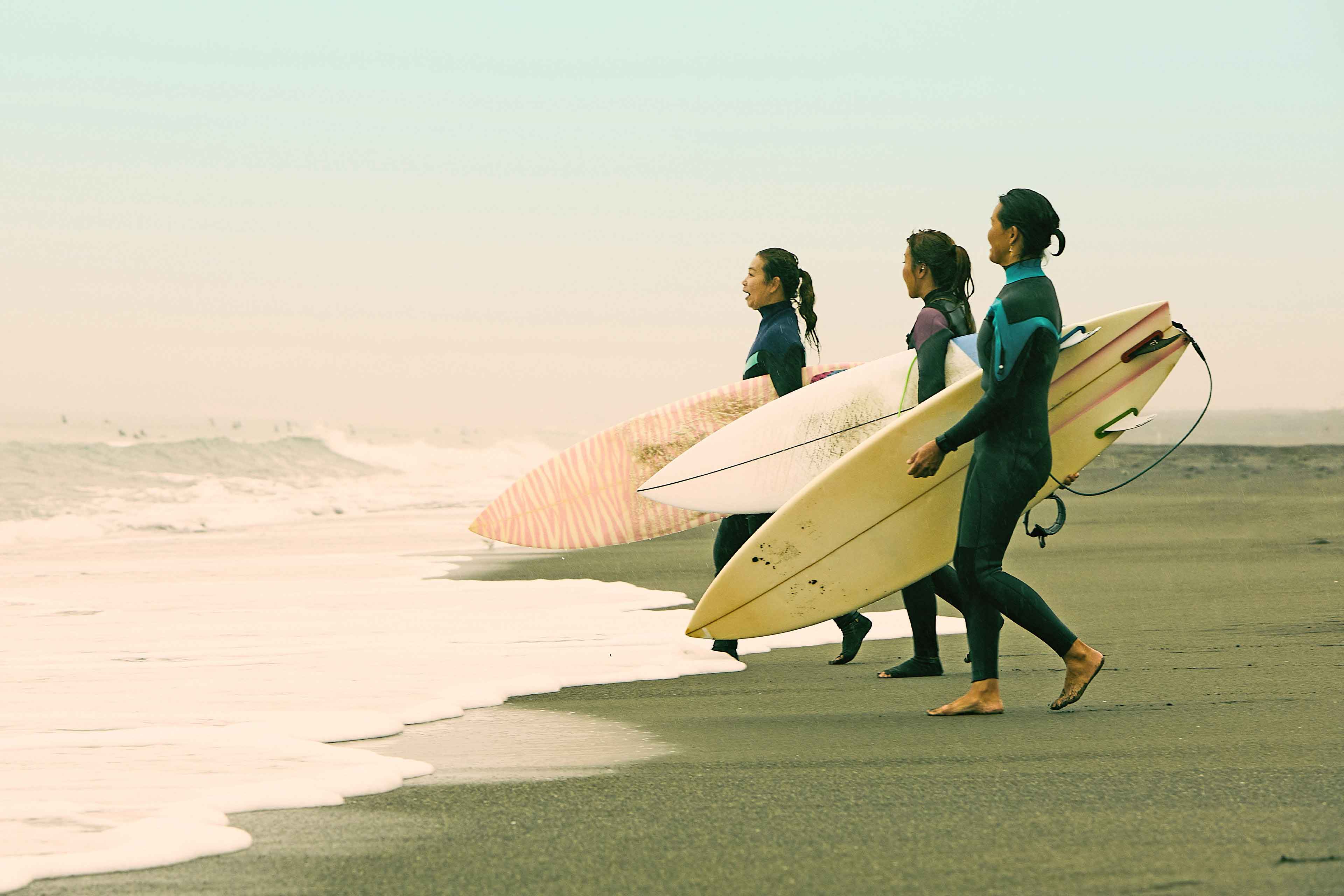 Surferinnen, die an einem regnerischen Tag an der Shonan-Küste Japans mit Surfbrettern zum Meer laufen