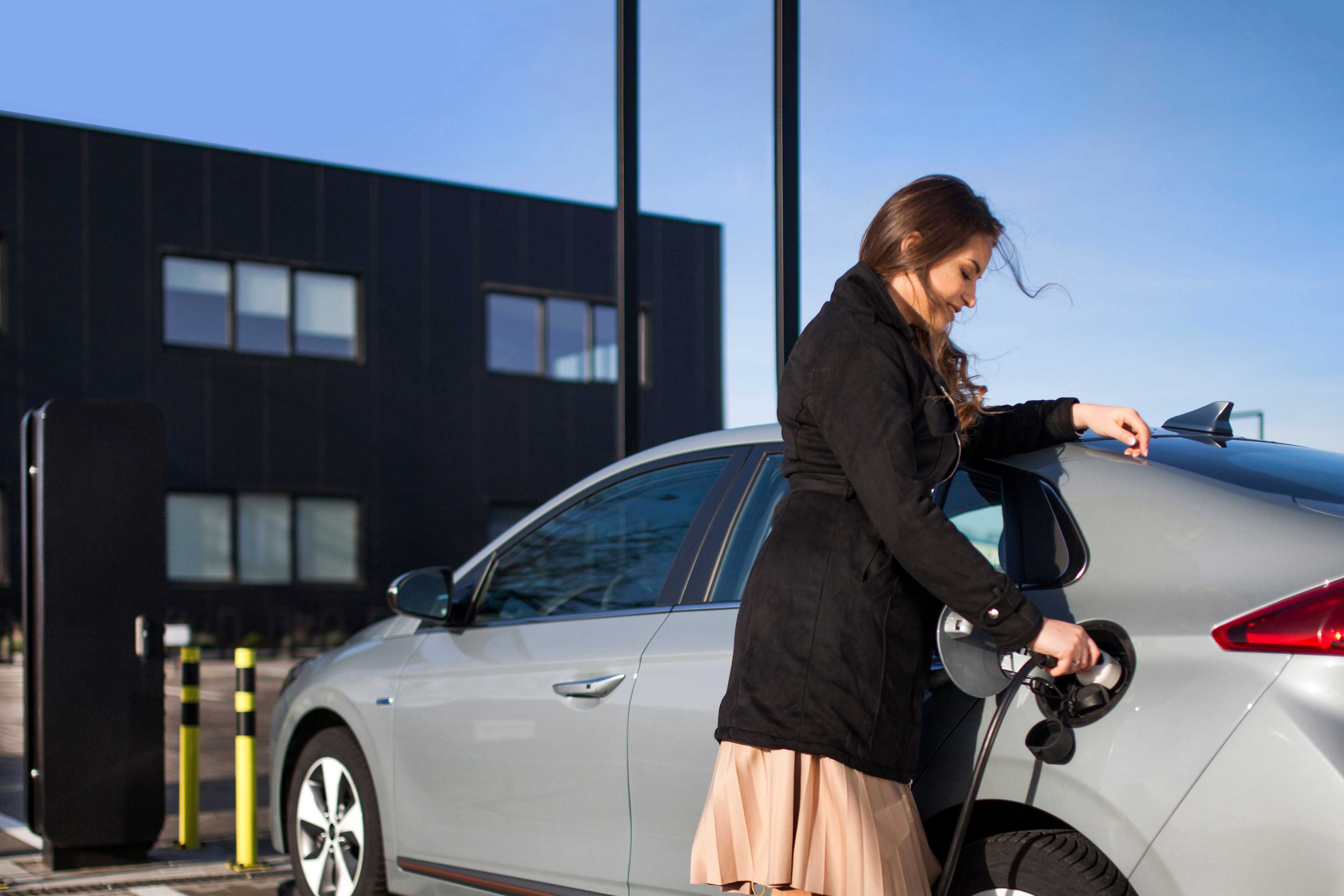 Junge Frau auf einem Parkplatz, die ihr Elektroauto auflädt