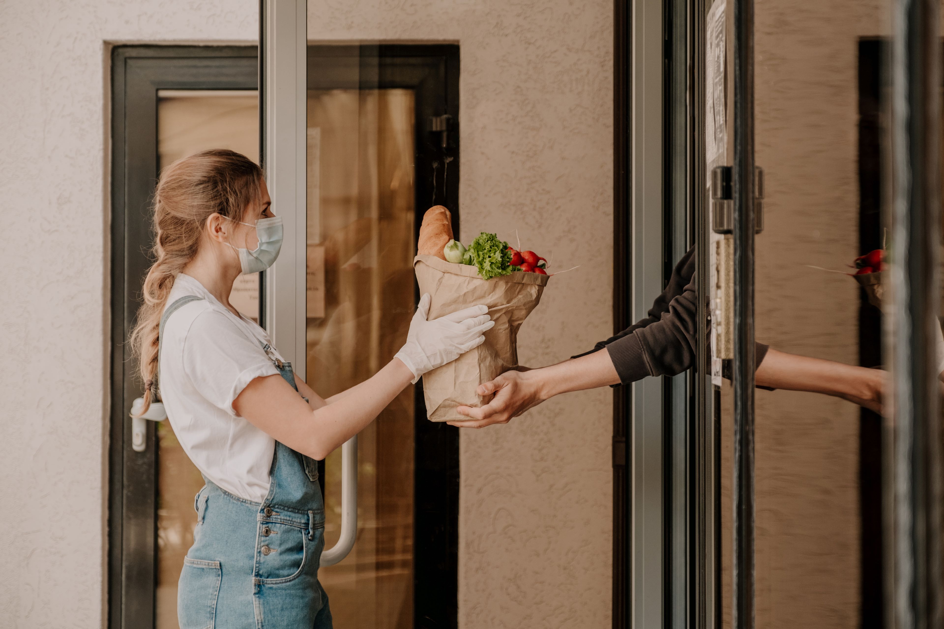 Woman in mask delivering food to man