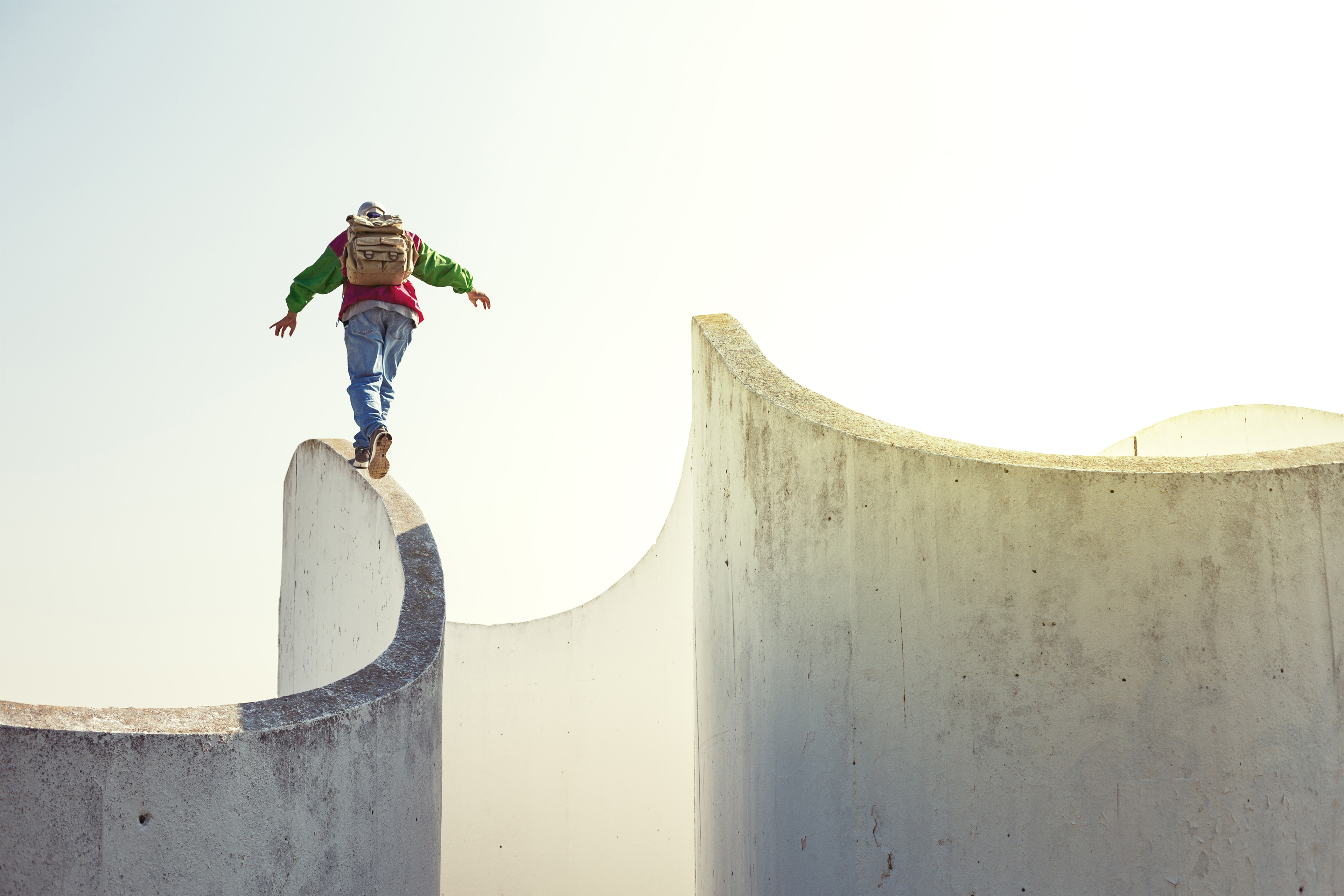 Man with backpack walking on a thin concrete wall