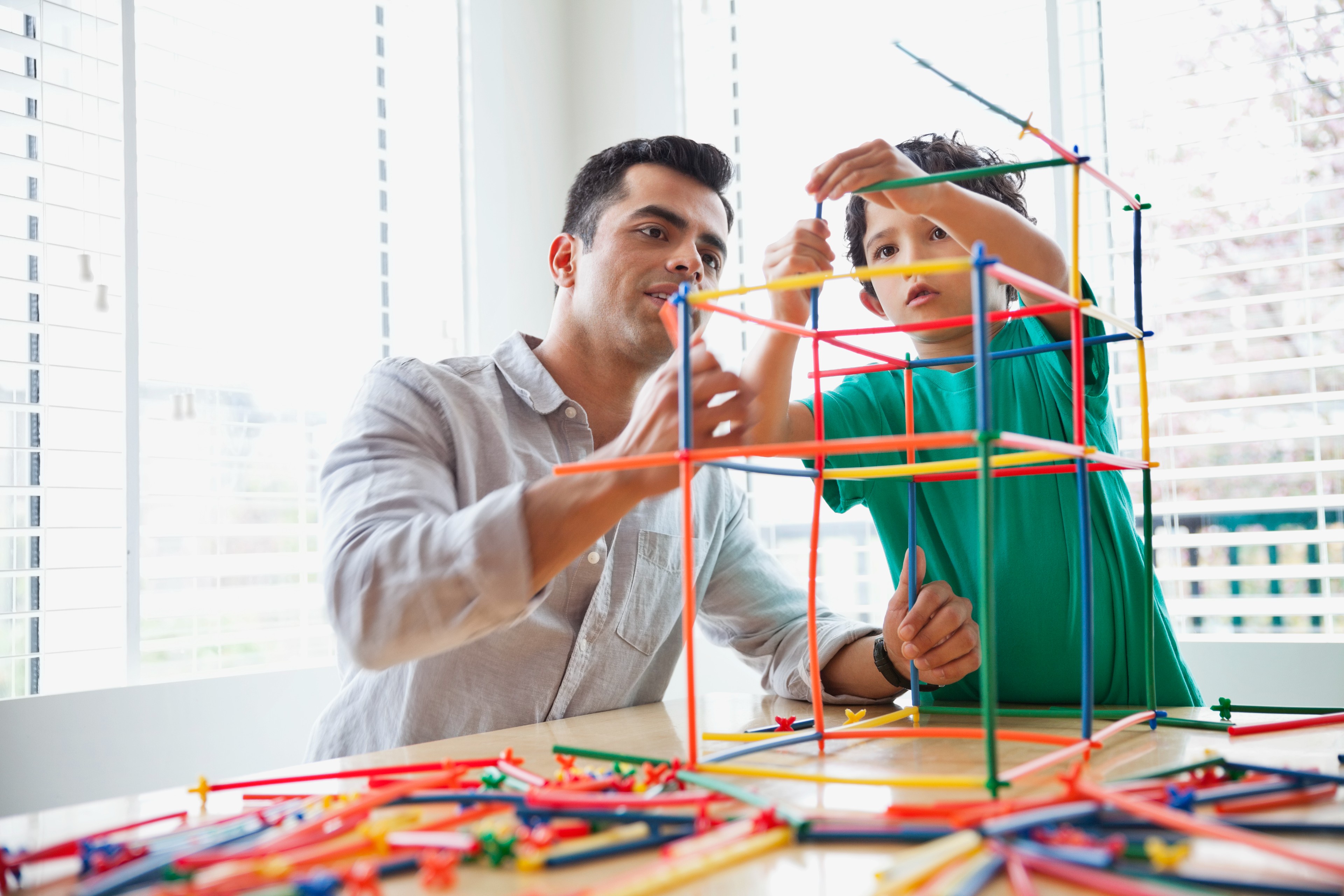 Father and son building a structure with colorful plastic sticks.