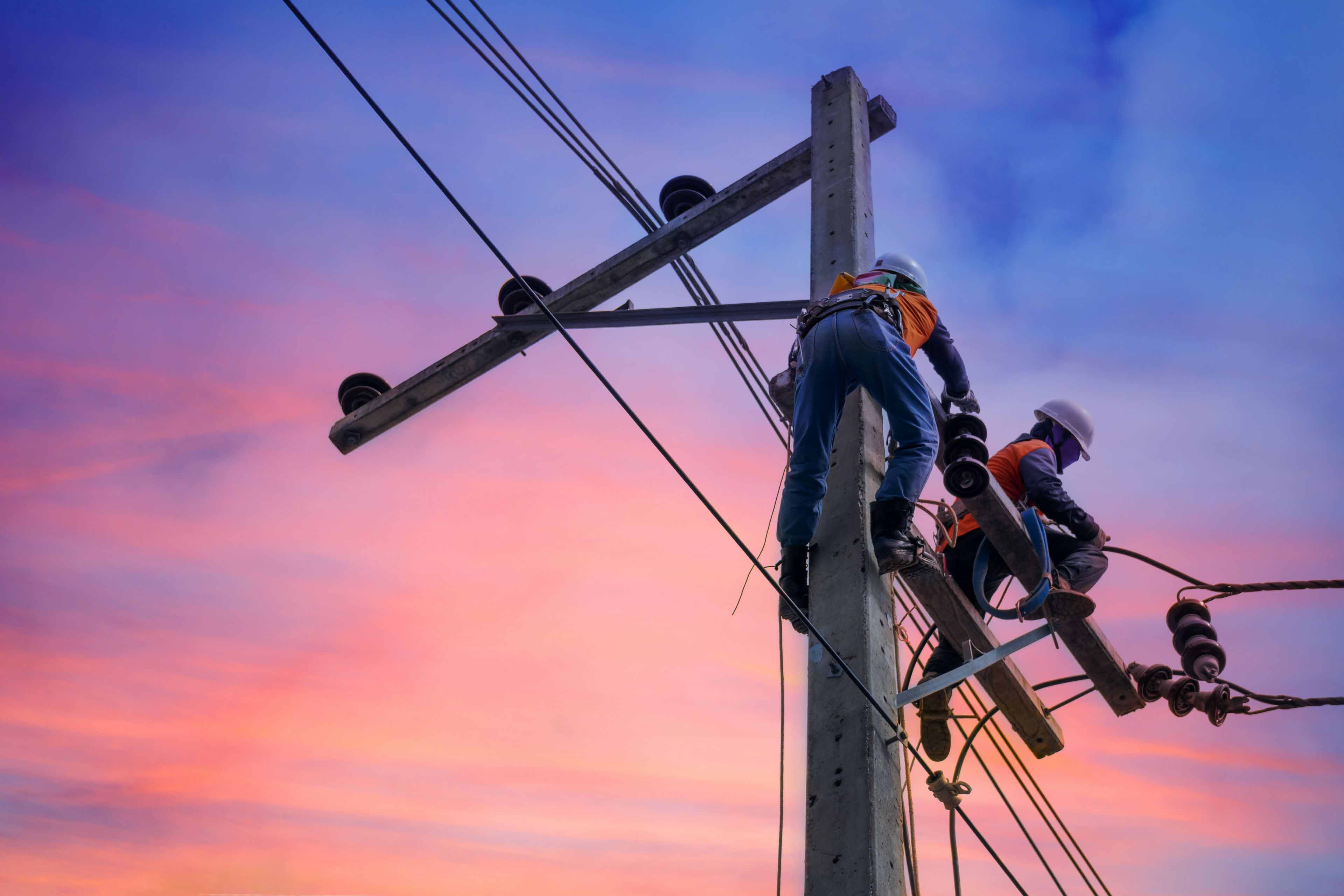 Two electrical workers on a power pole during sunset.