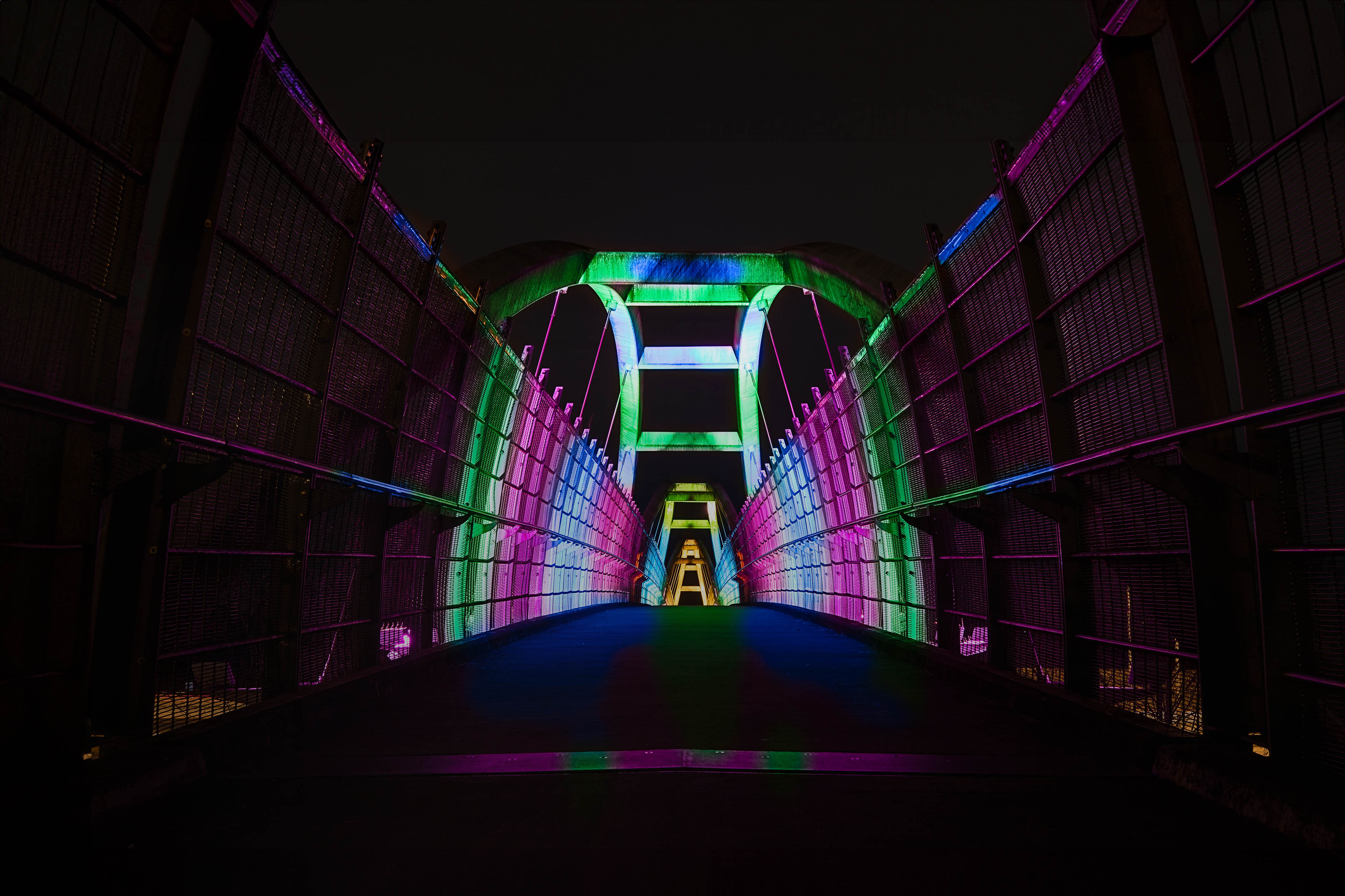 Bright colors illuminate pedestrian walkway over highway at night