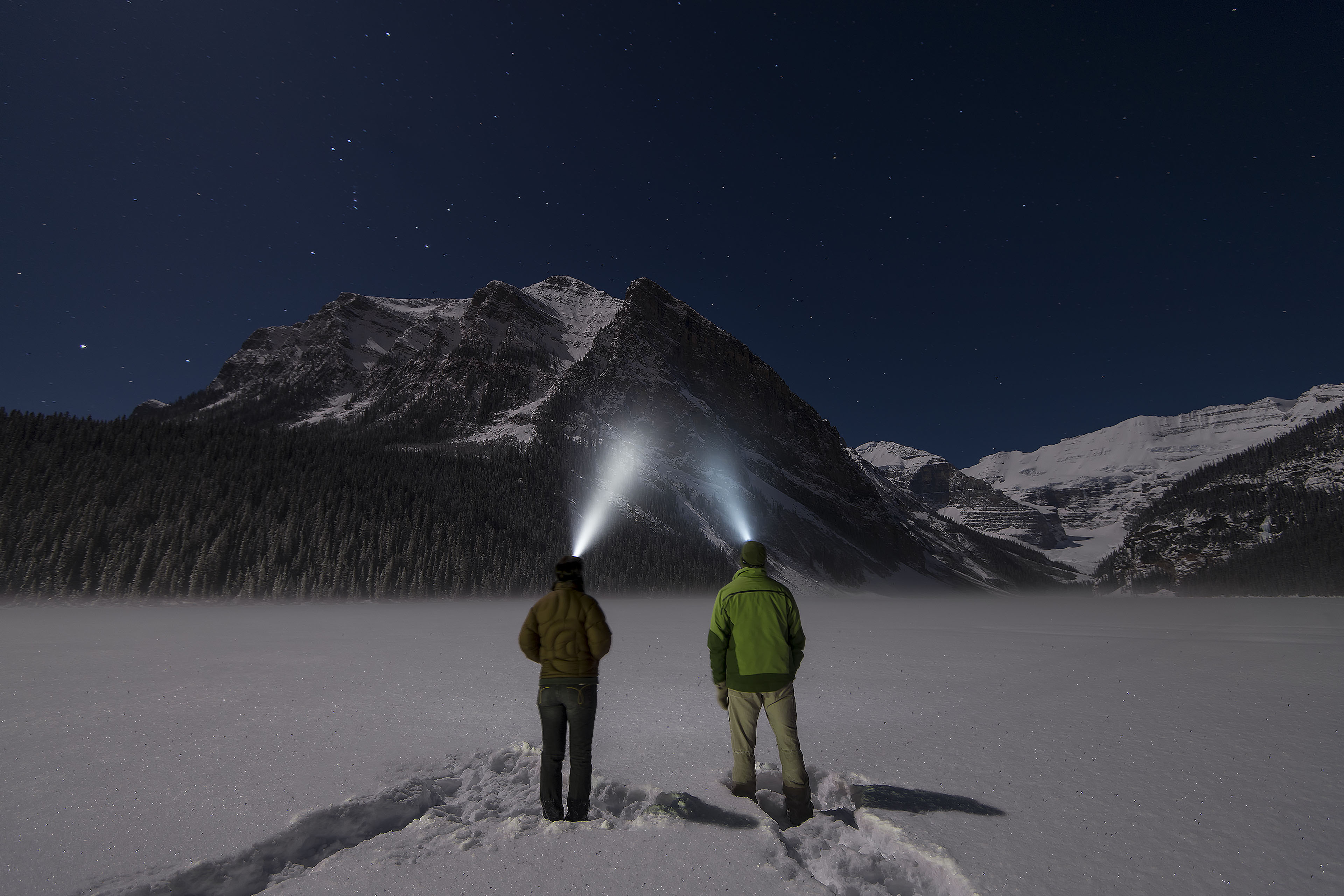 Ey couple stand in snowy clearing with headlamps