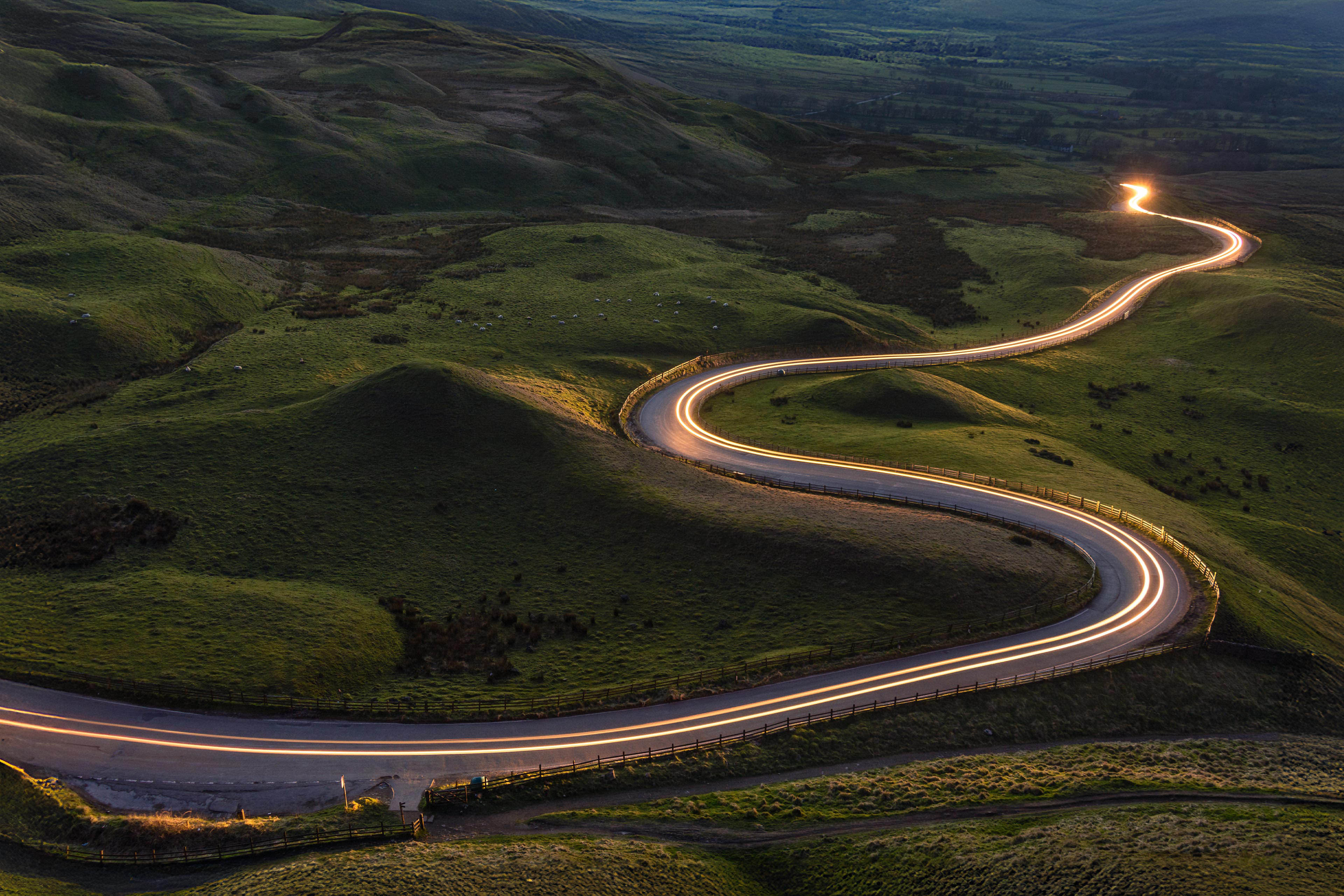 Winding curvy rural road with light trail from headlights leading through British countryside.