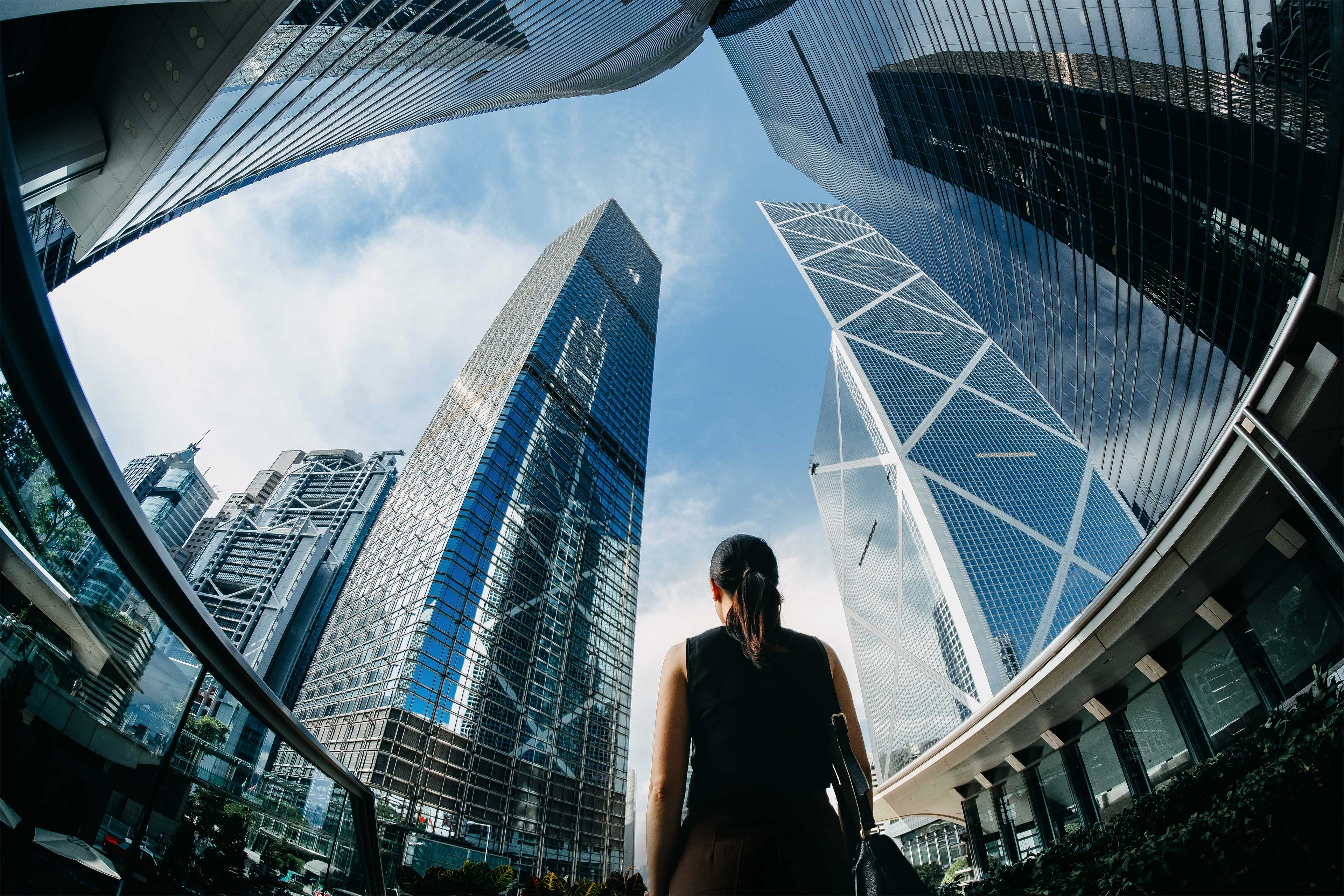 Rear view of businesswoman standing against contemporary financial skyscrapers in HK