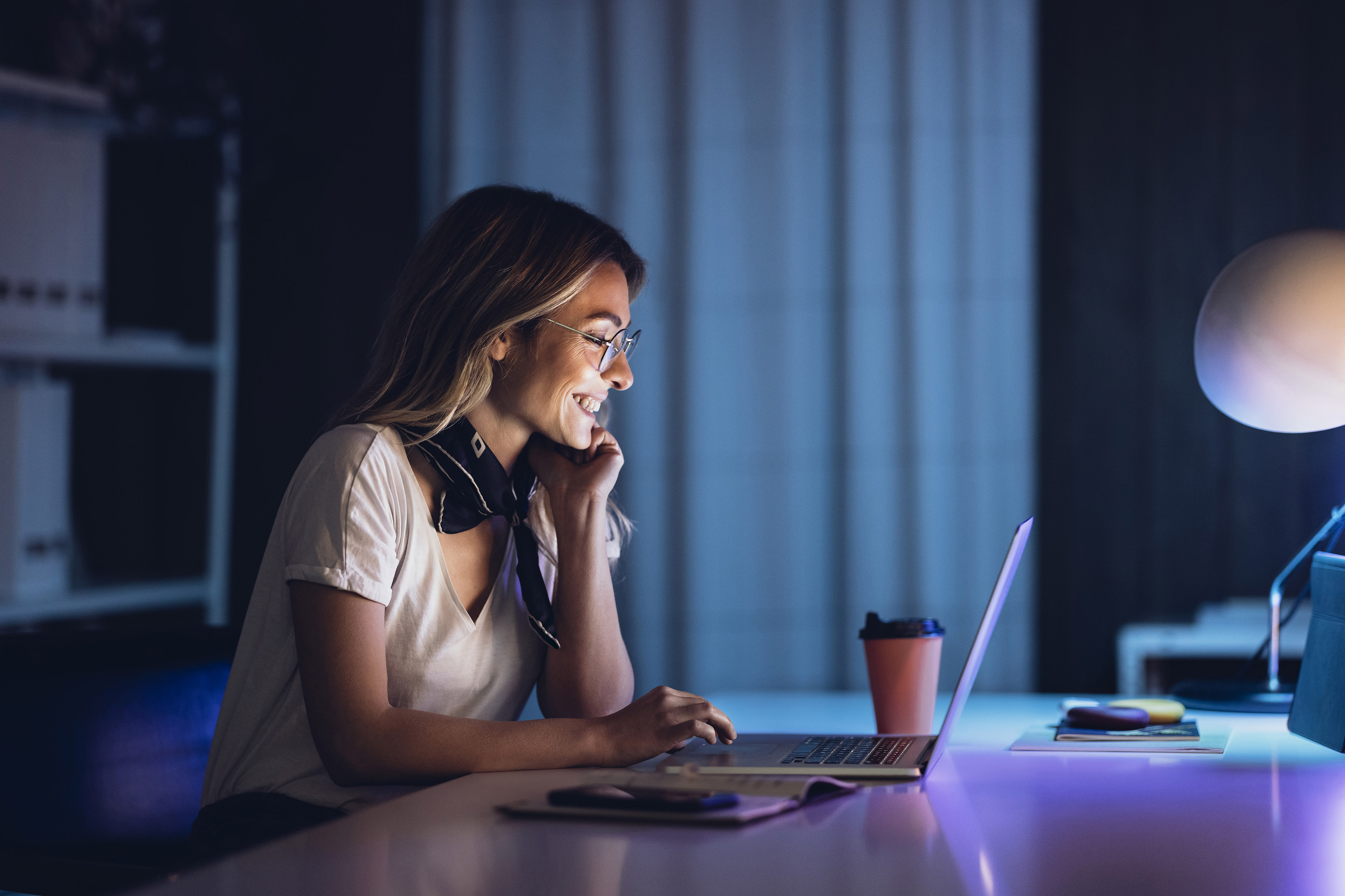 Cheerful lady with coffee and laptop in night