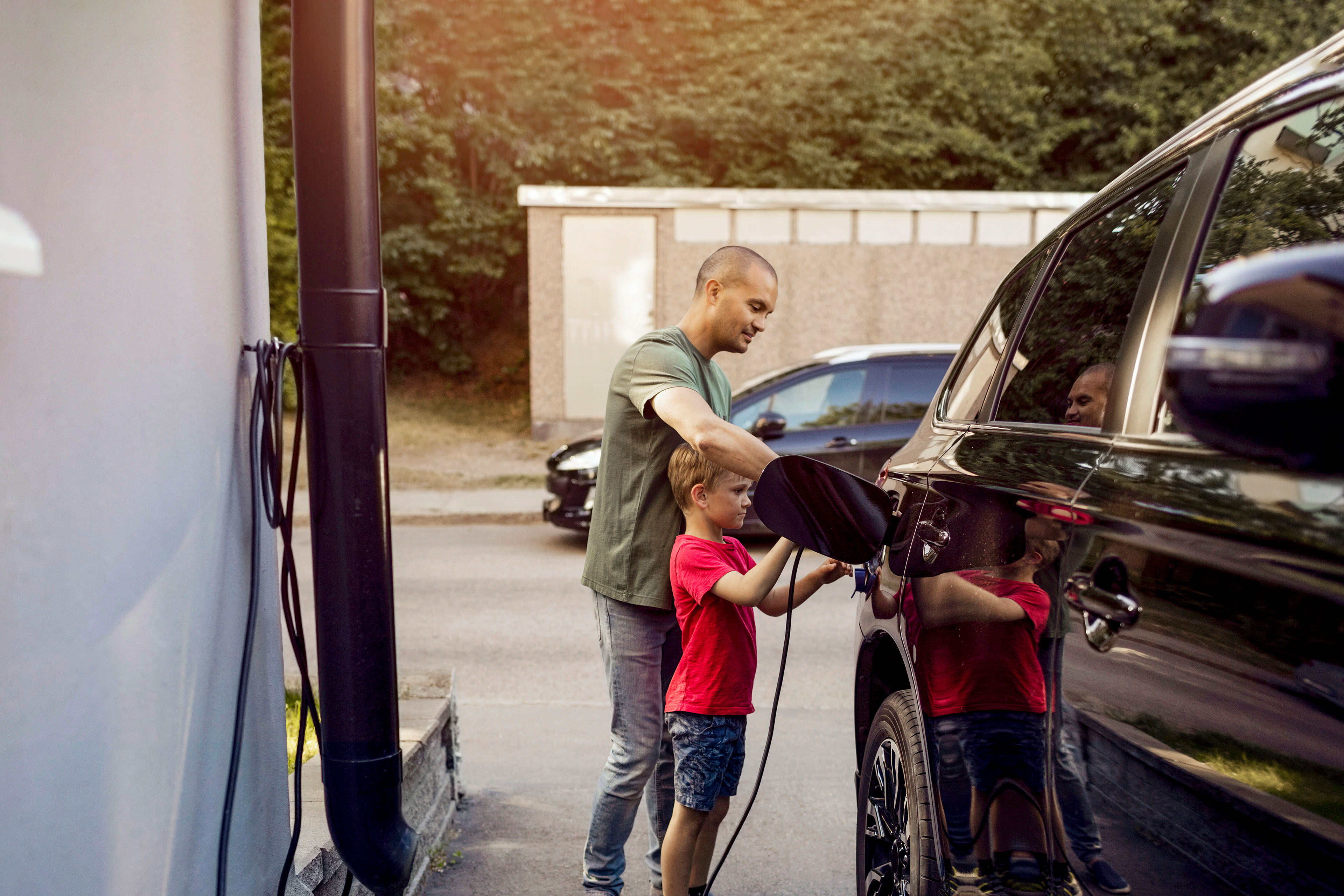 Father and son charging electric car outside home