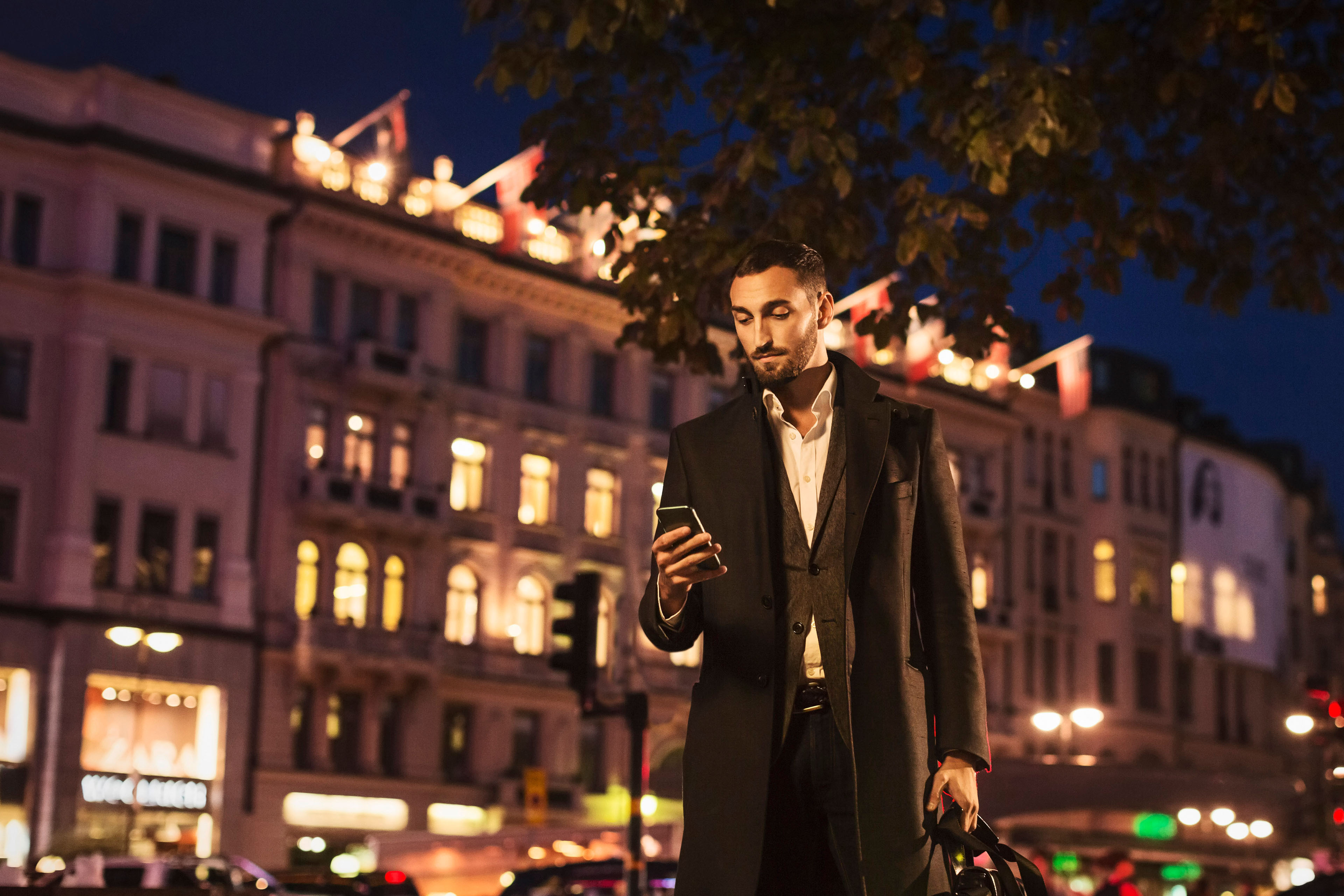 Young man using smart phone while standing on city street at night