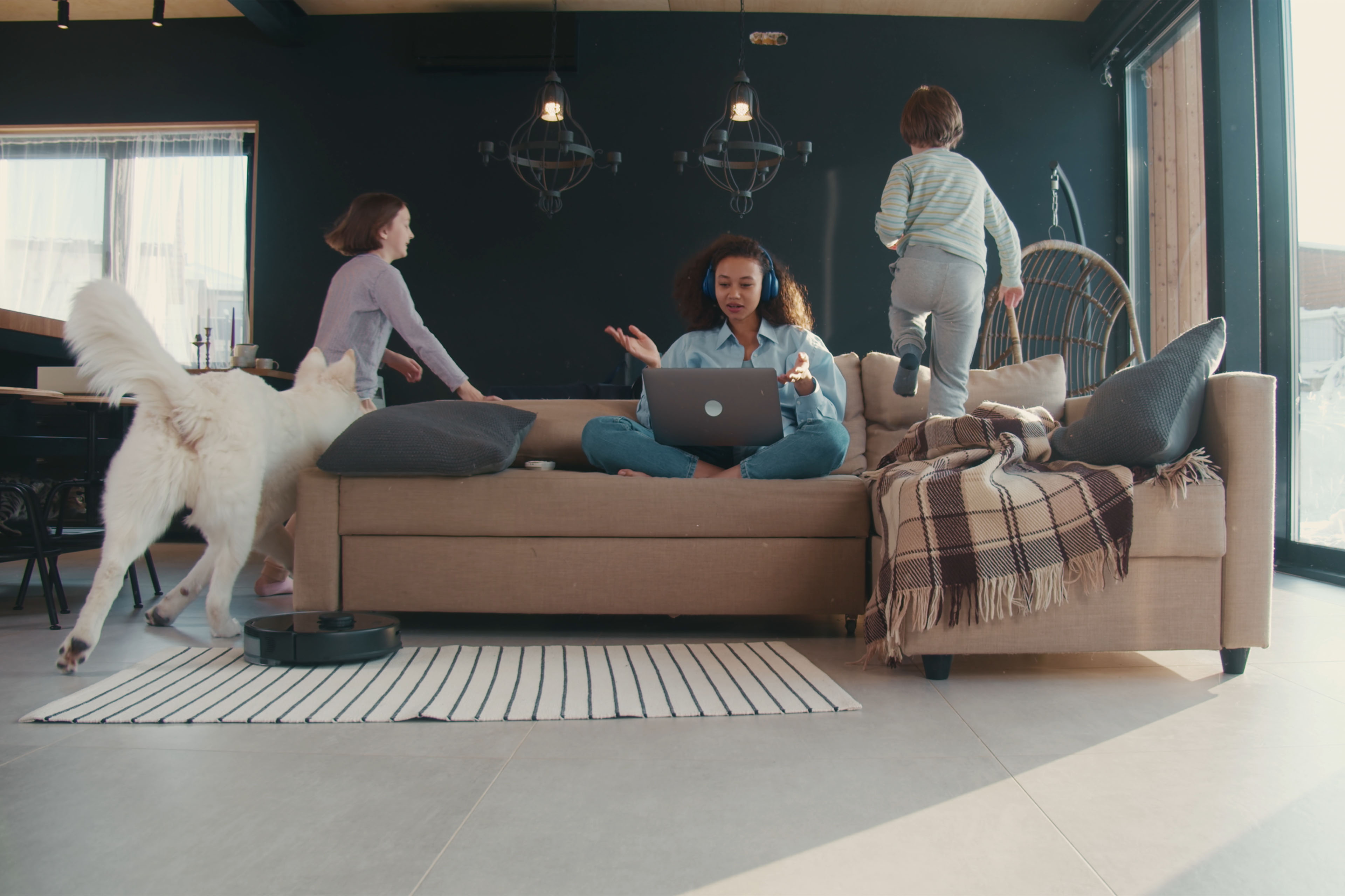 Woman working and kids running around sofa