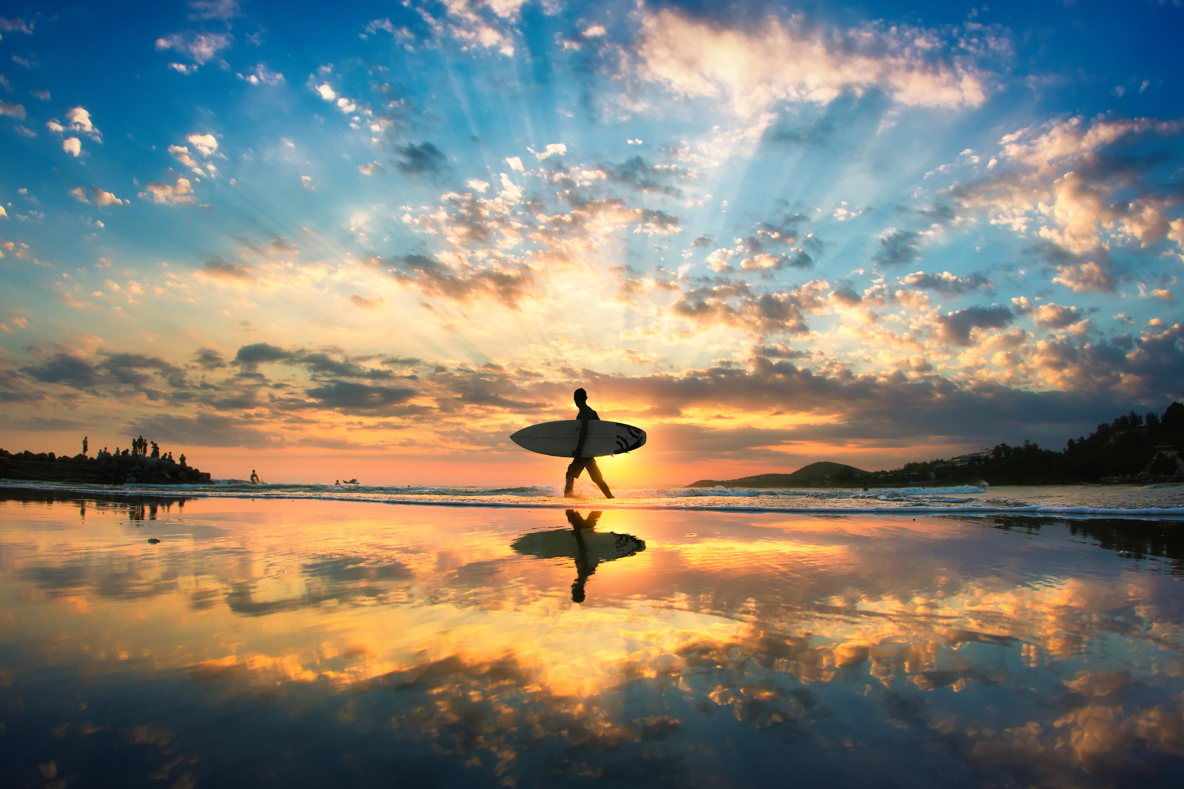 A man is walking with a surf in his hands across the sea shore