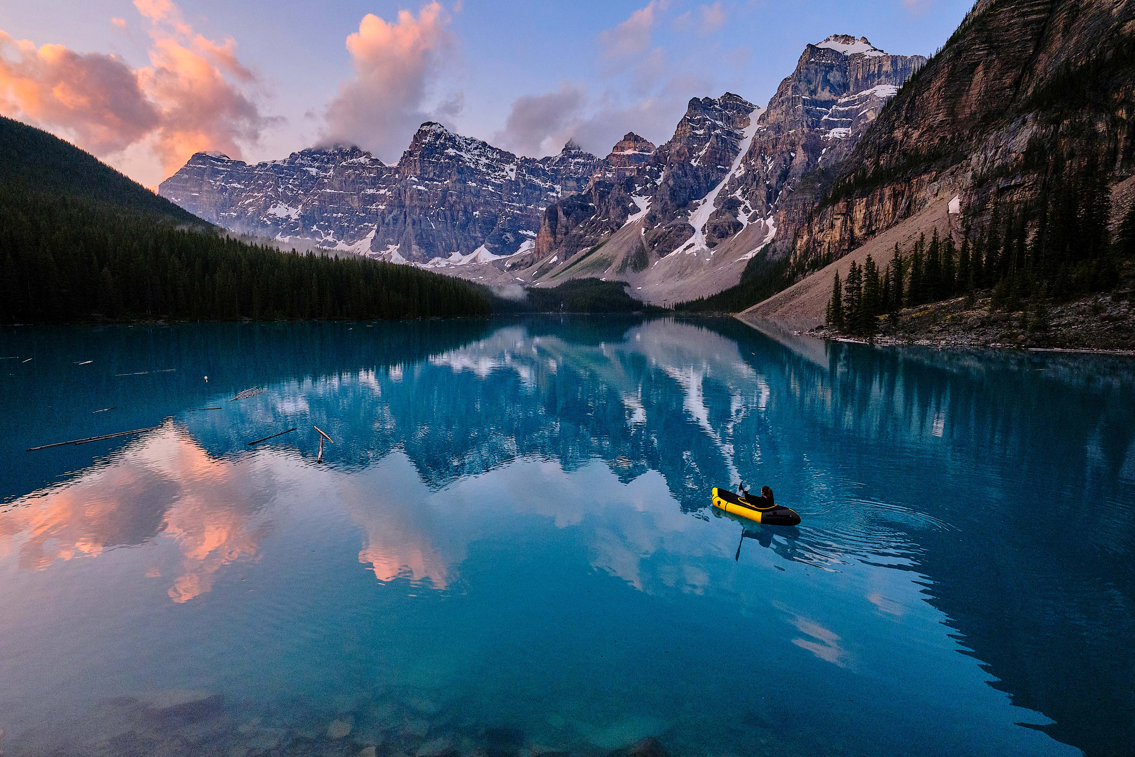 Young woman kayaks across mountain lake at sunrise