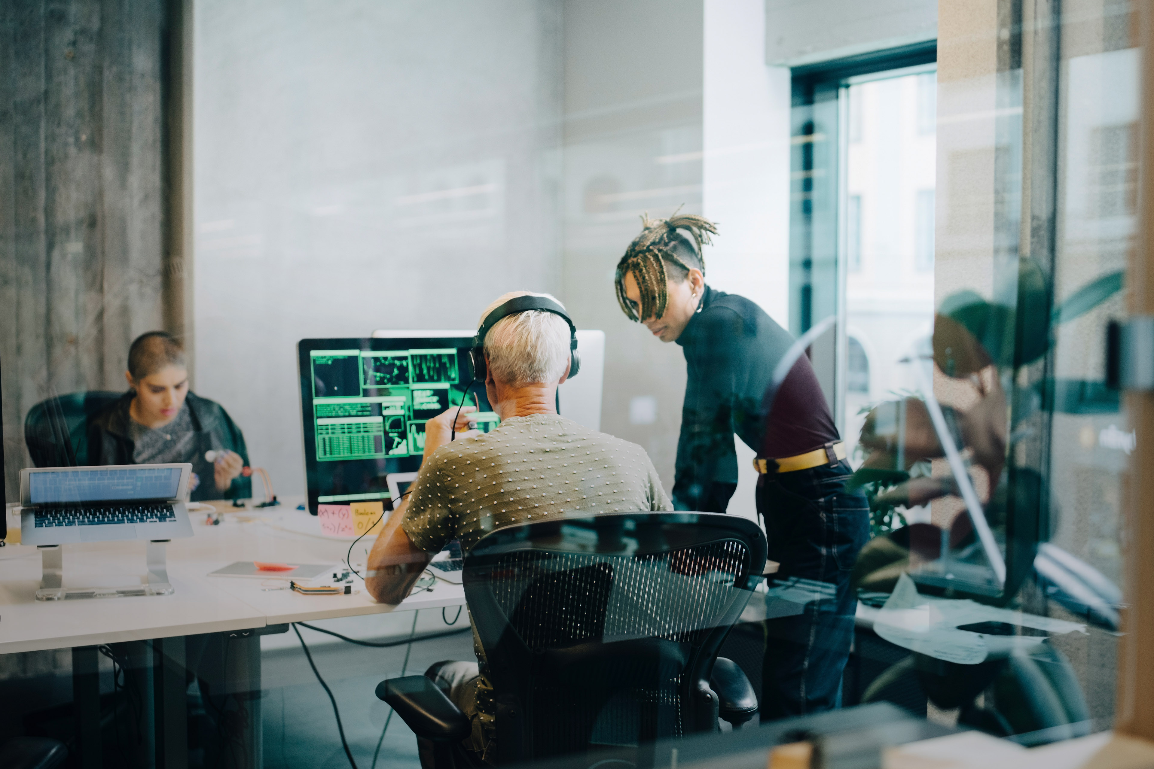 Male engineer discussing with colleague while coding over computer at office