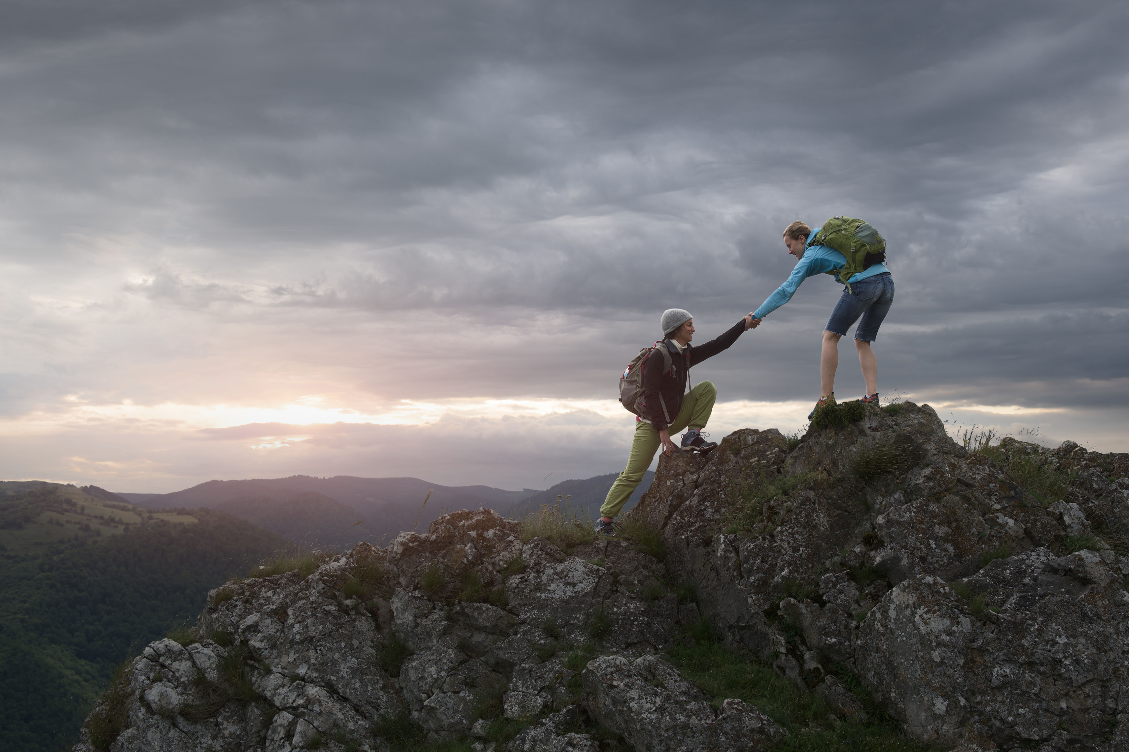 hiker woman helping her friend reach the top of the mountain