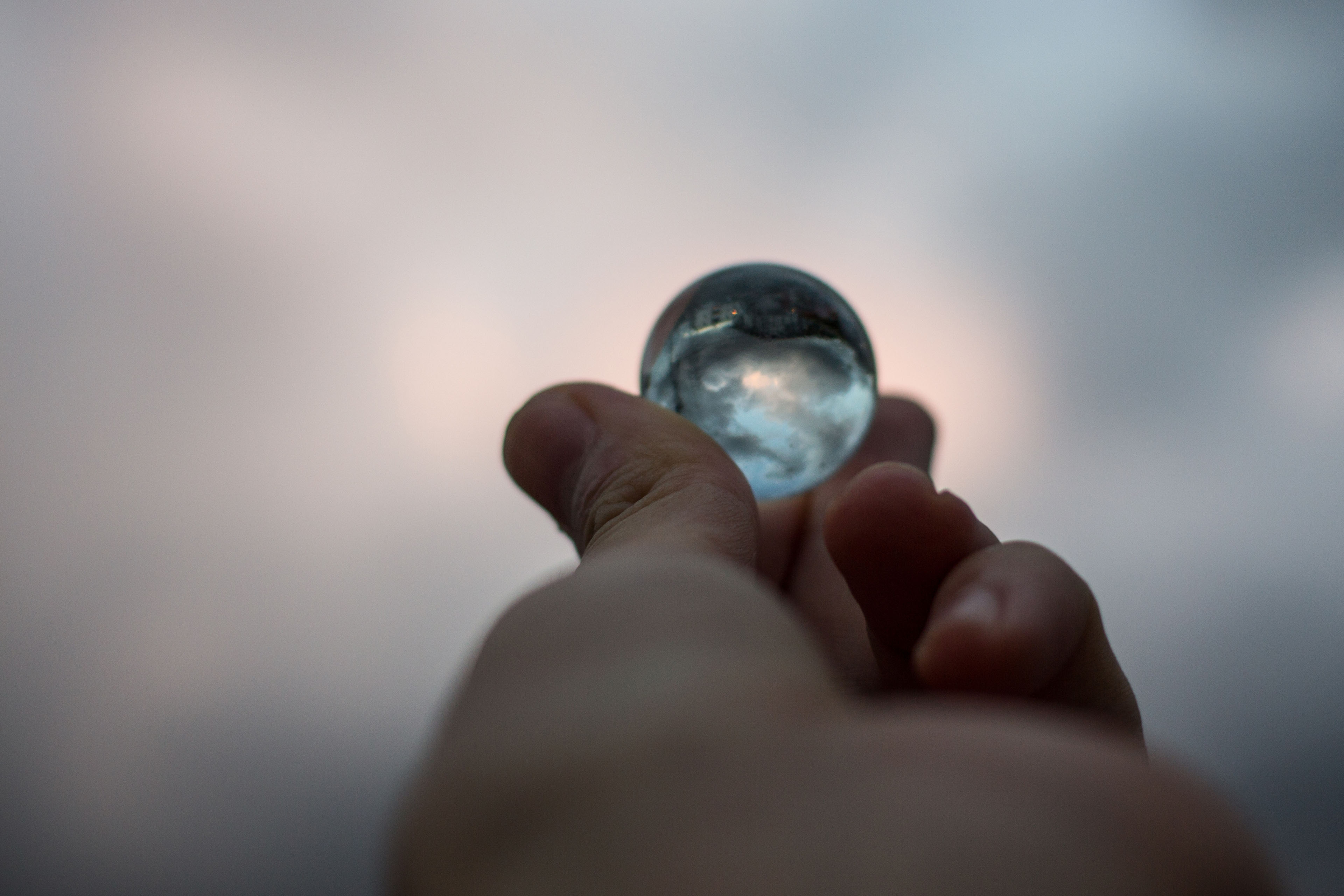 close up of hand holding marble against sky at dusk