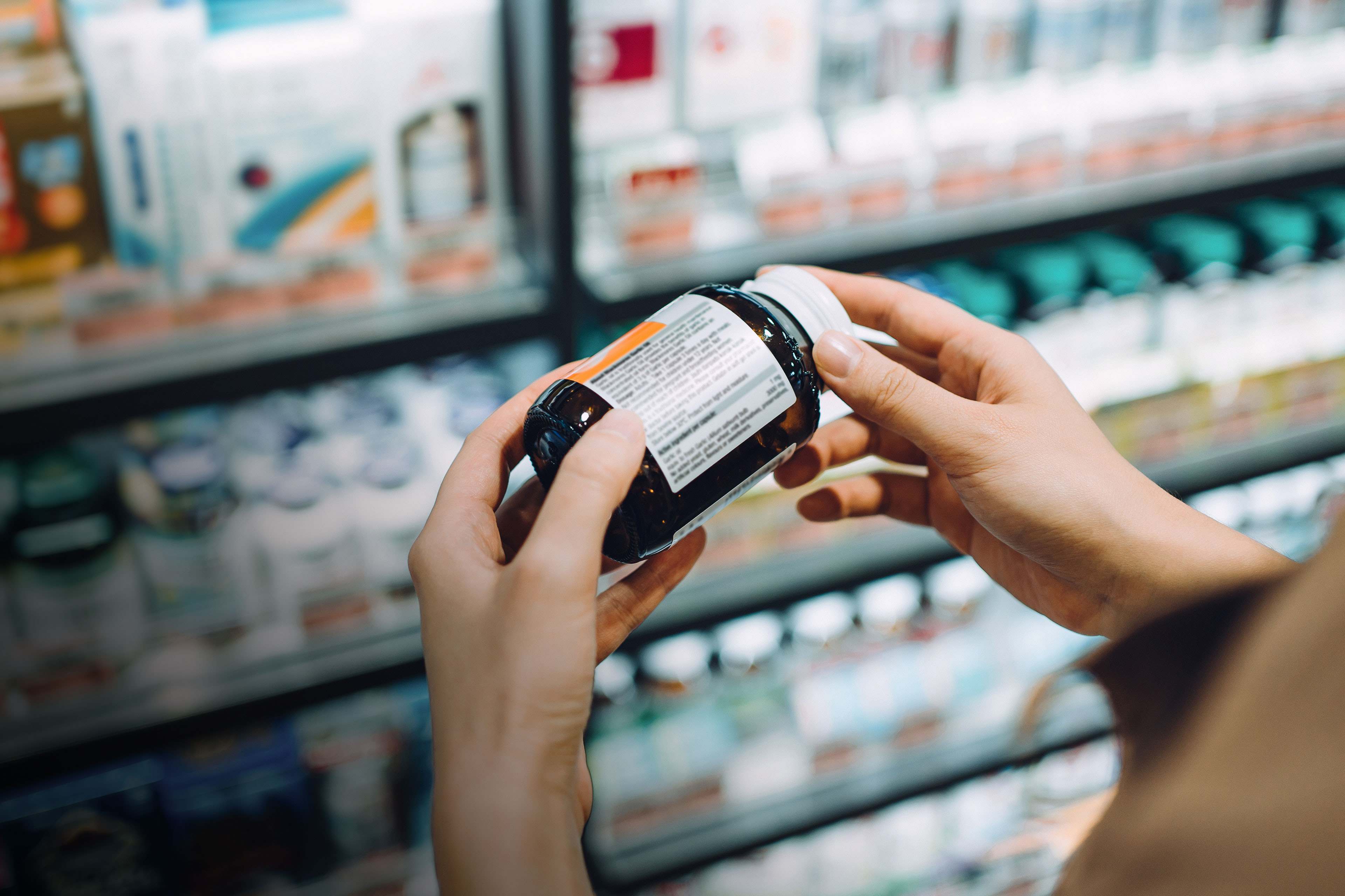 Asian woman reading the label on a bottle of medicine in a pharmacy