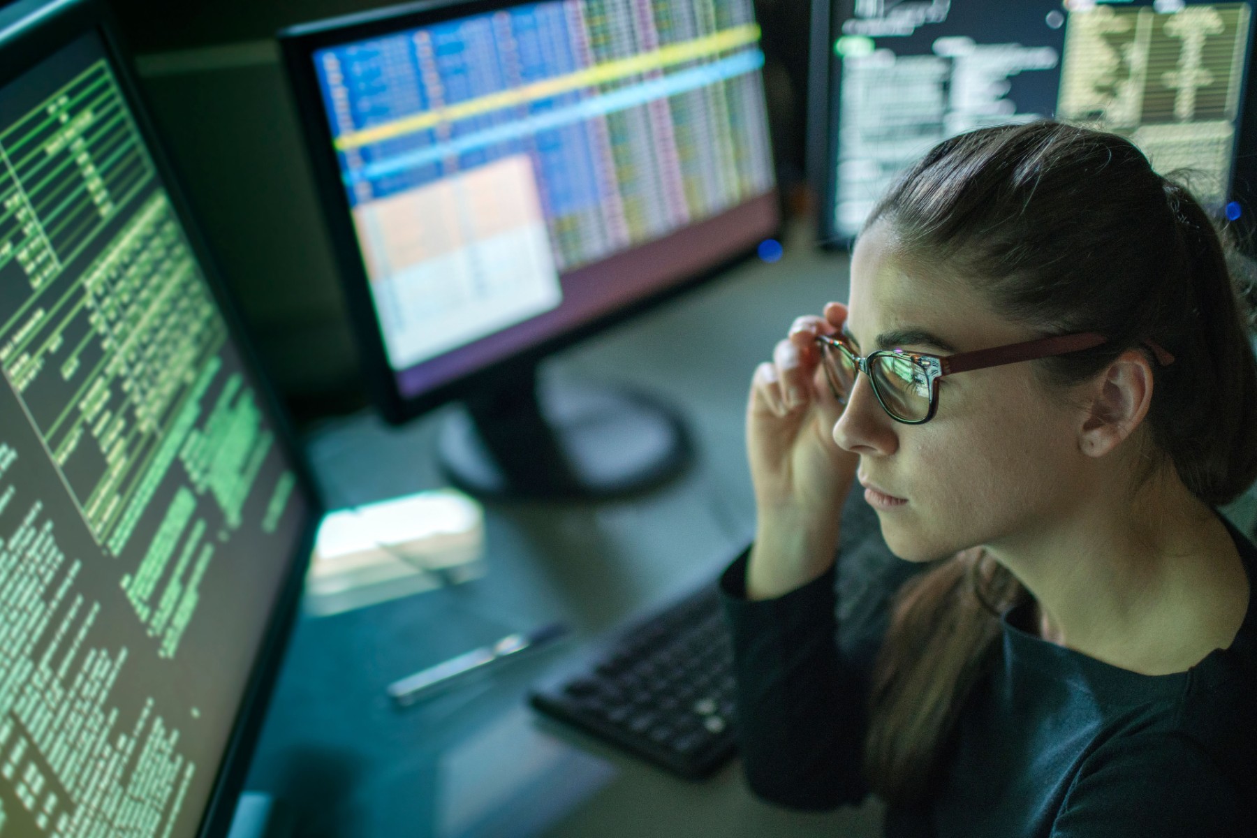 Woman in dark room looking at screens displaying computer code