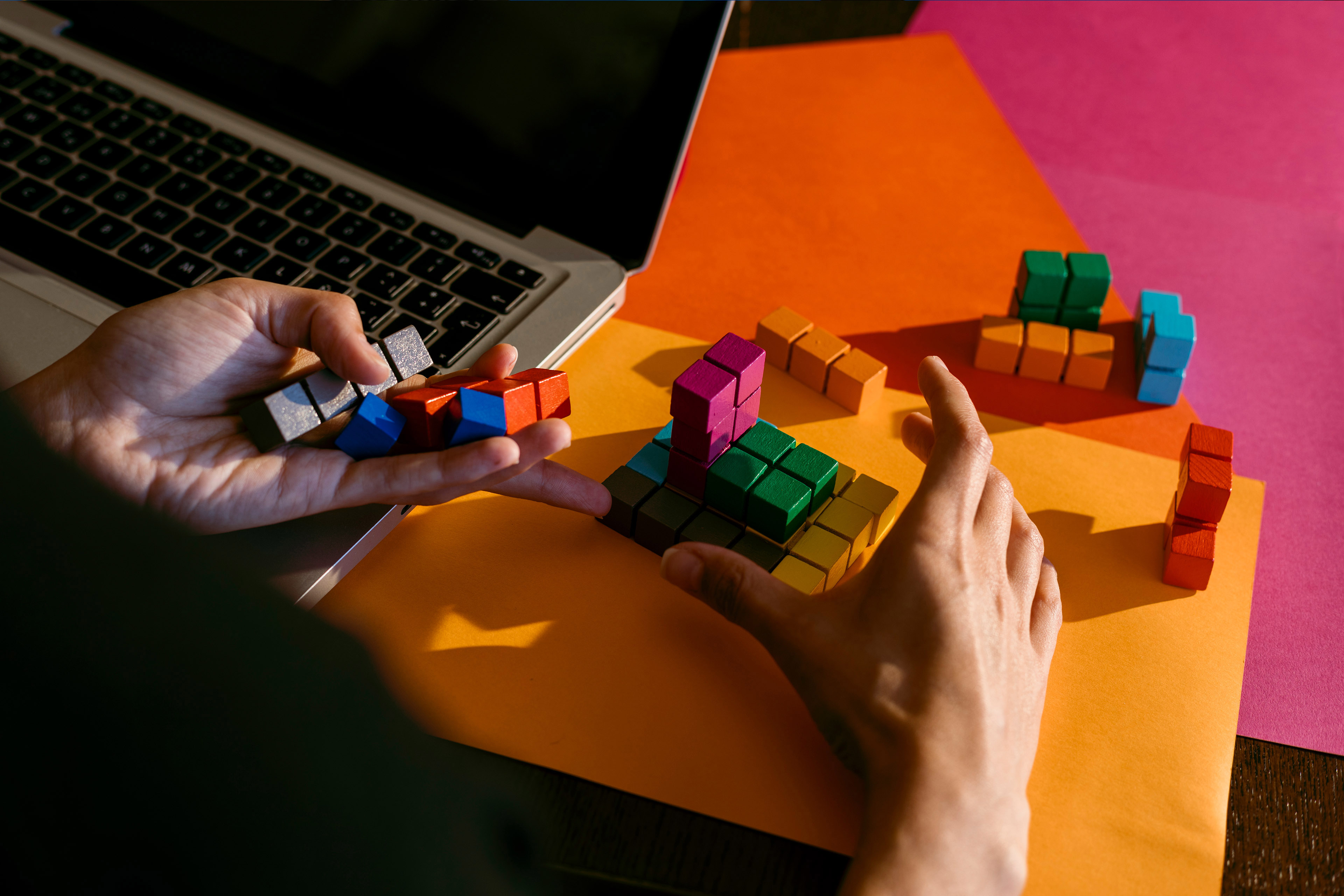 Hands of businesswoman playing with colorful toy blocks by laptop at table