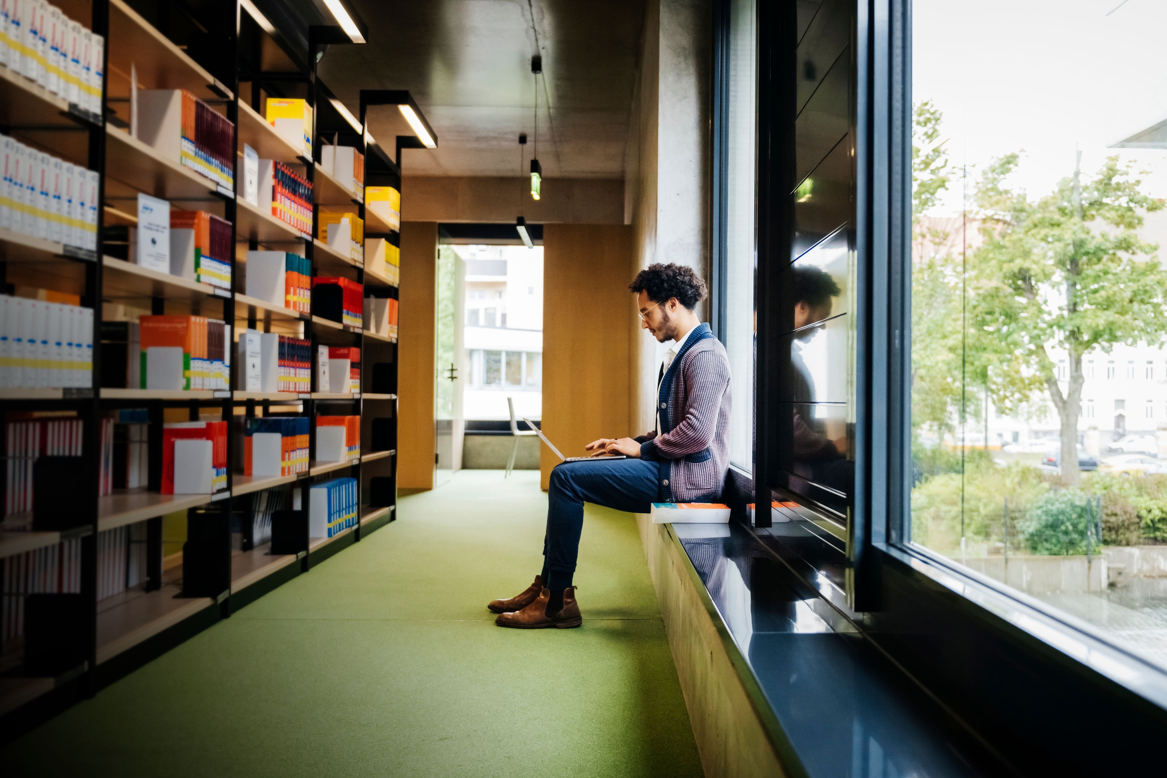 A man sitting by large window working in library