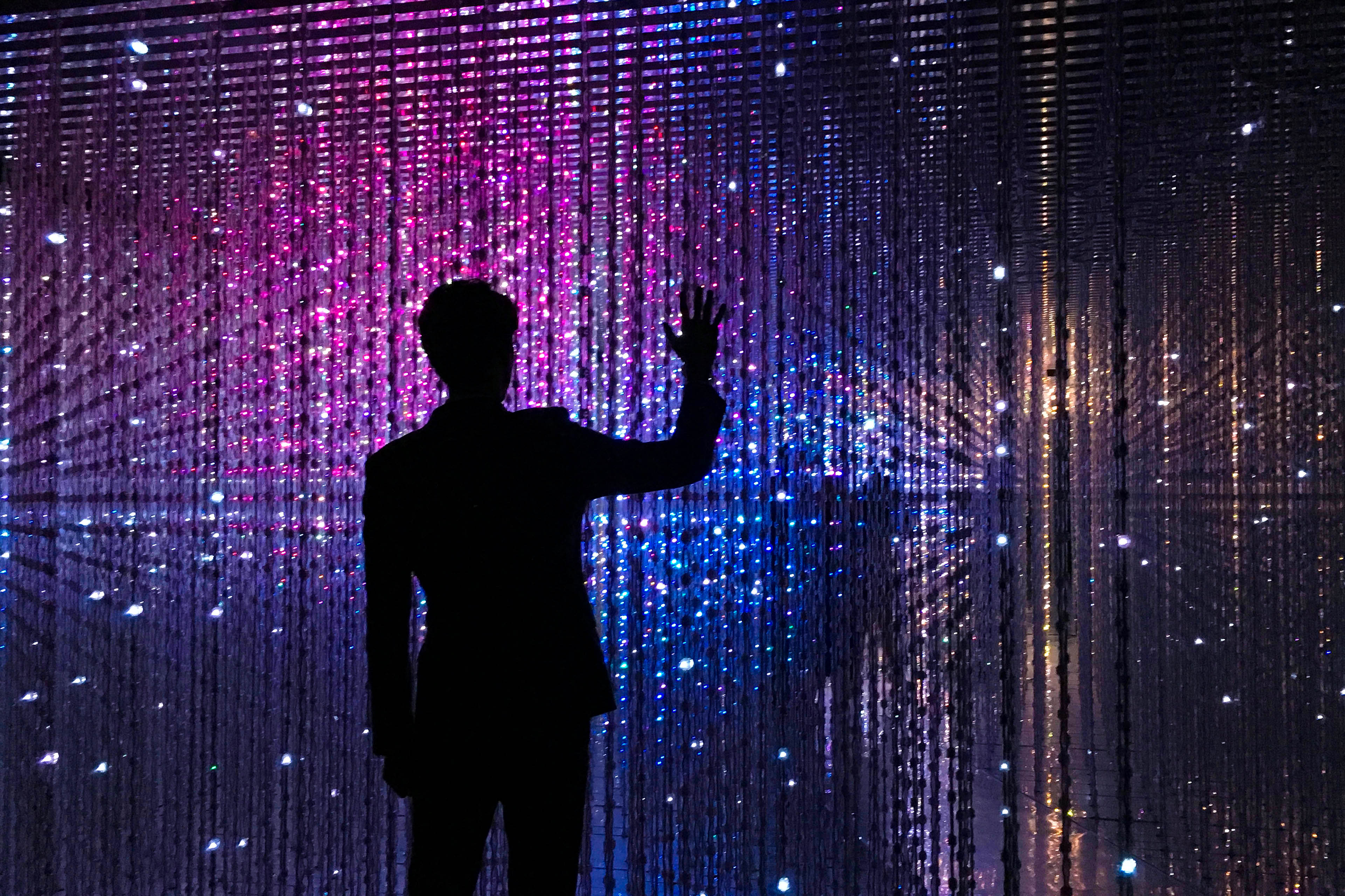 Rear view of a man standing against an illuminated wall