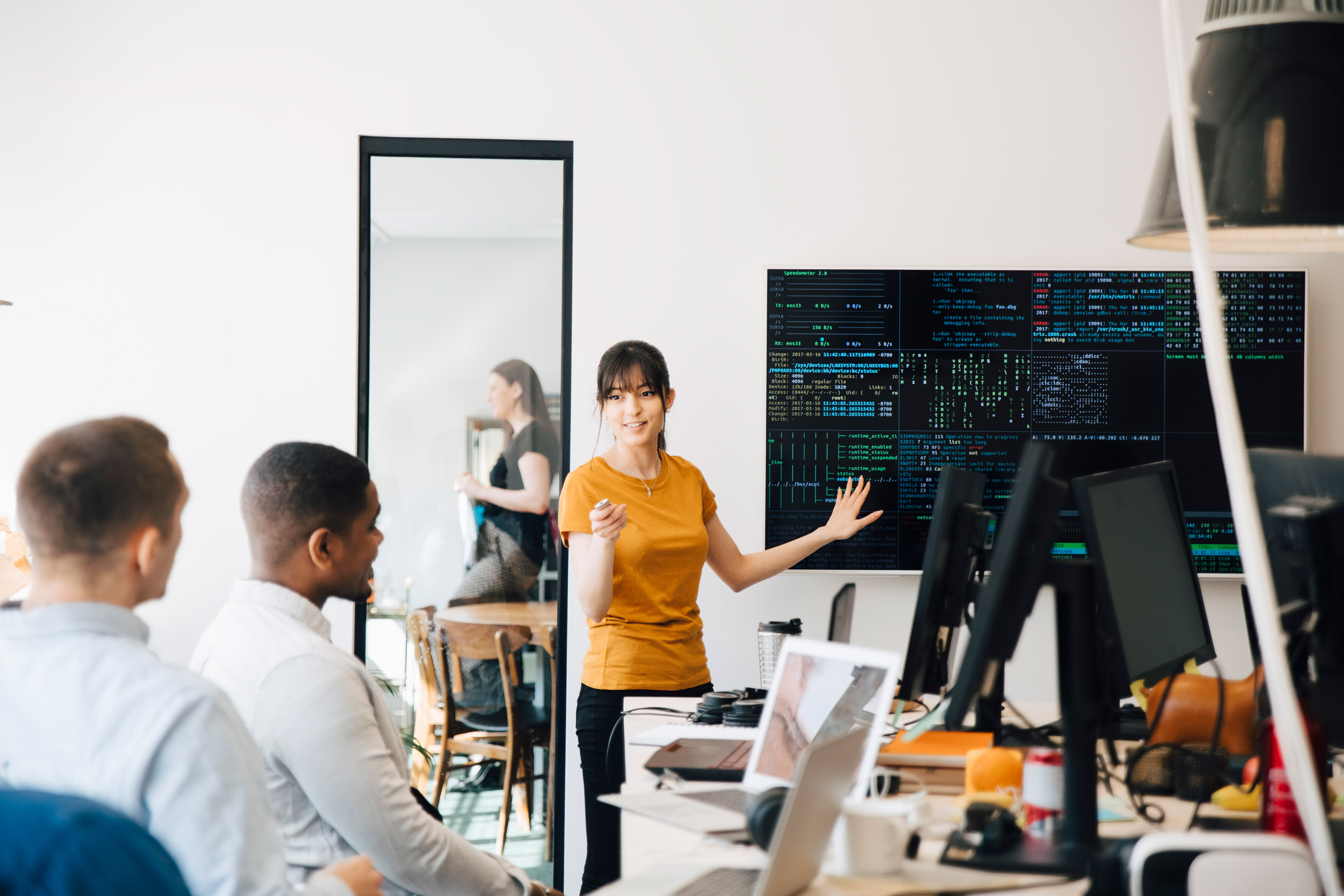 Female programmer interacting with colleagues while giving presentation in office