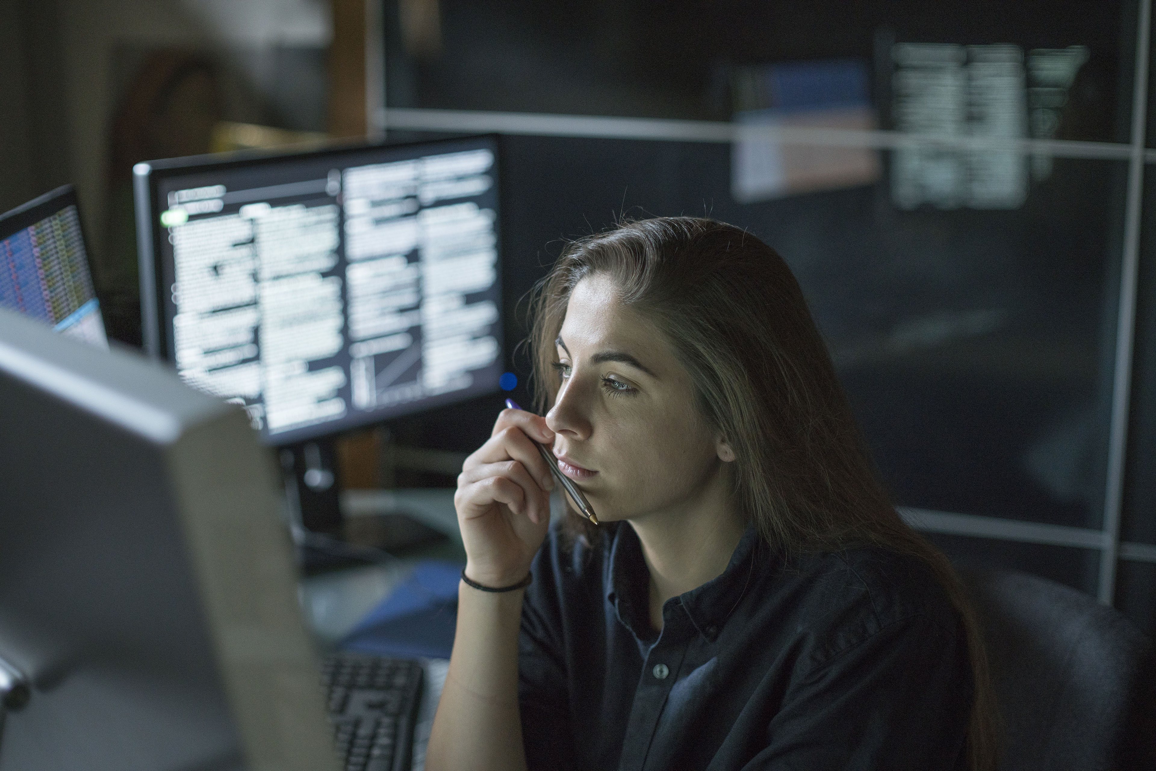 A woman seated at a desk surrounded by monitors displaying data