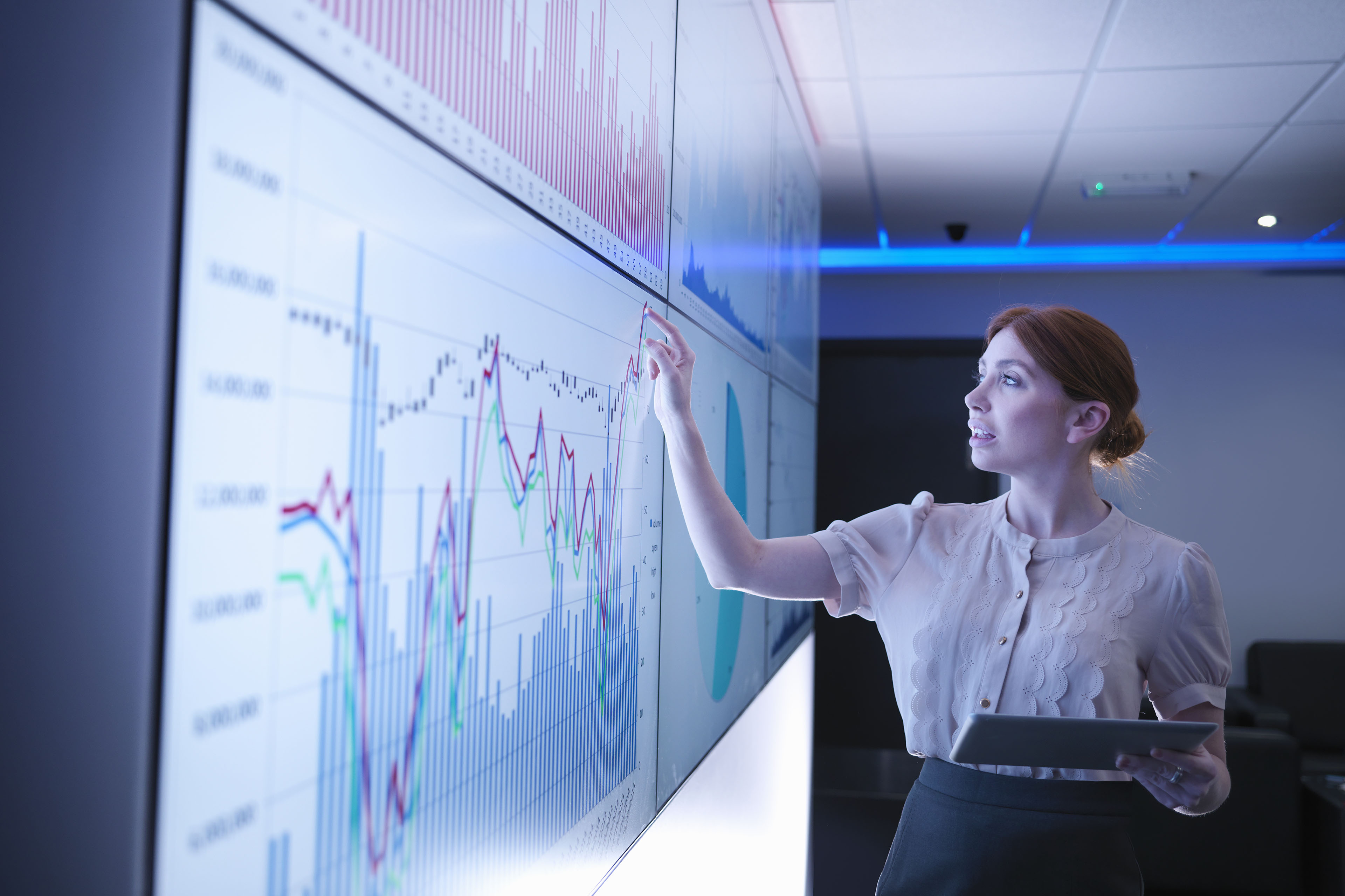 Business woman studying graphs on screens with a tablet