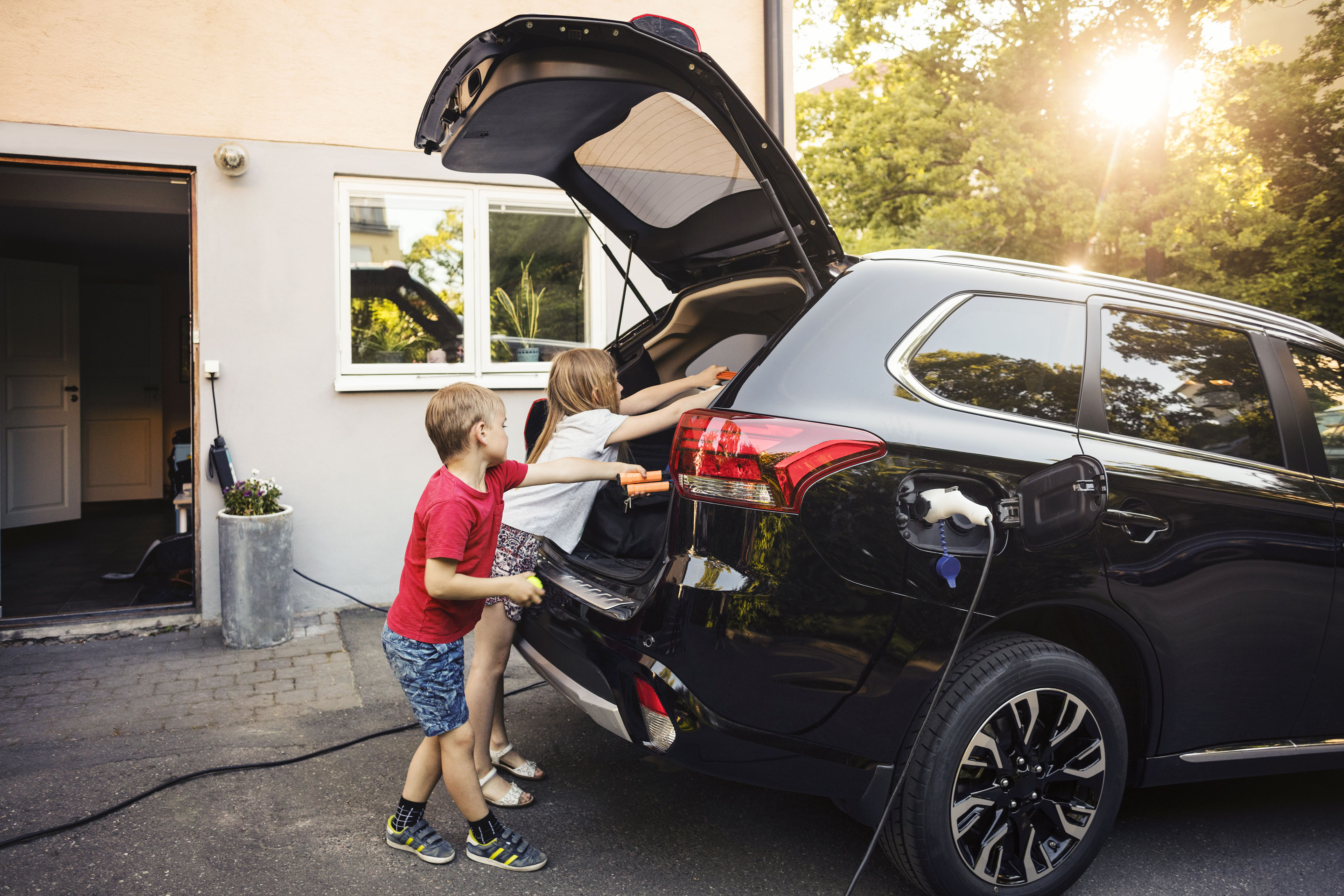 Kids loading black electric car trunk against house in back yard