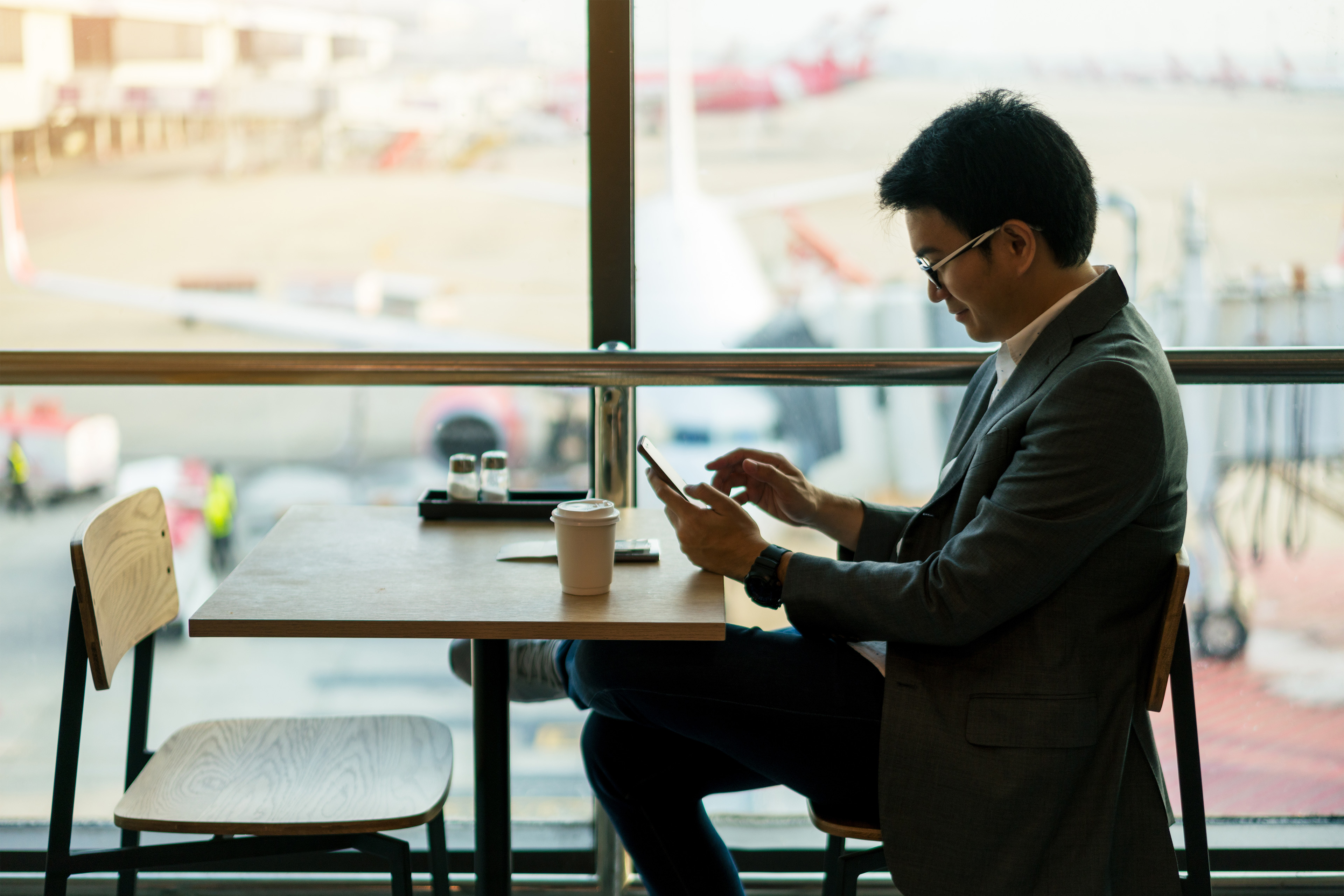 A man sitting in cafeteria and looking into his phone and smiling