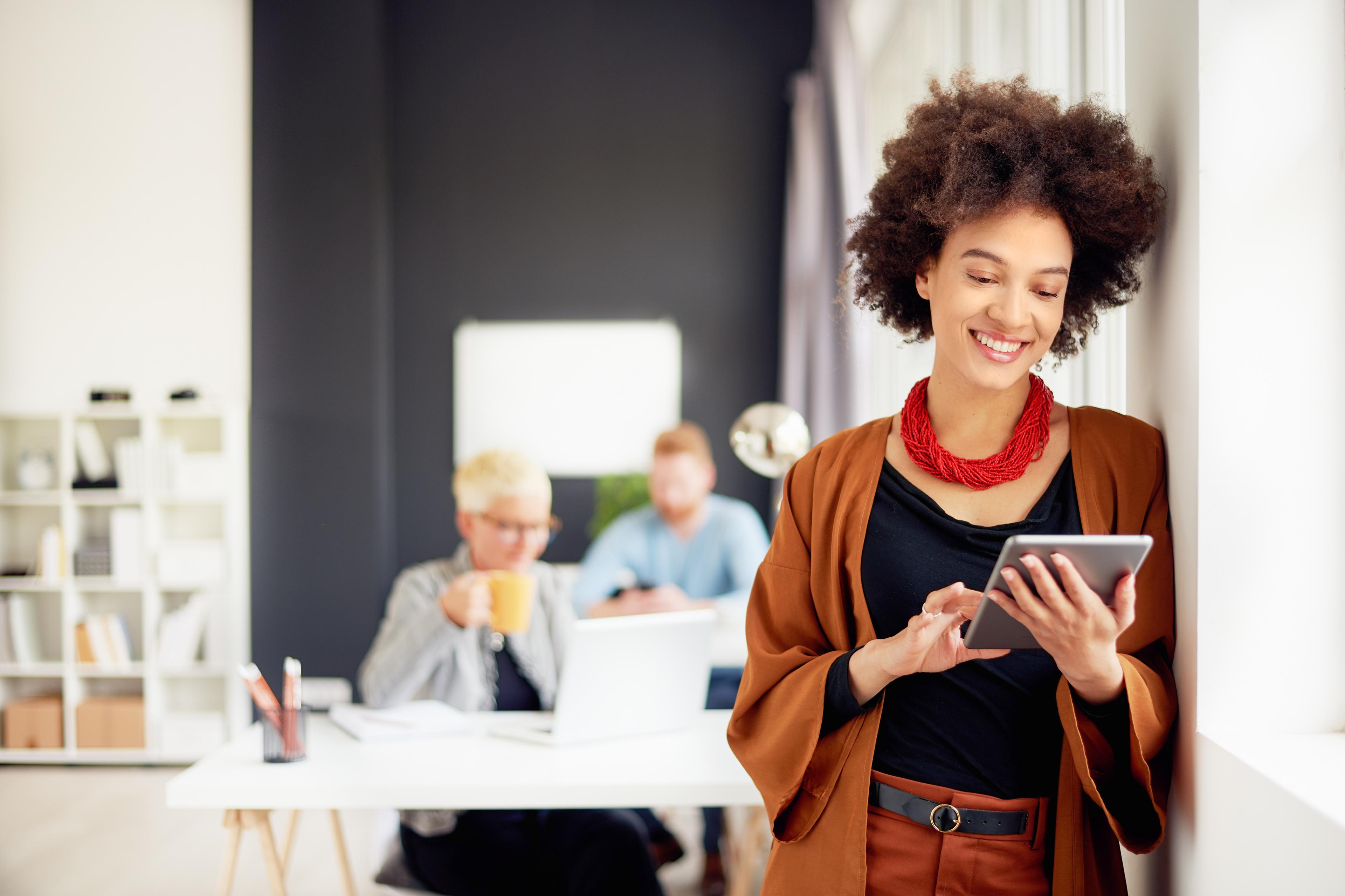 African american businesswoman standing in modern office and using tablet device