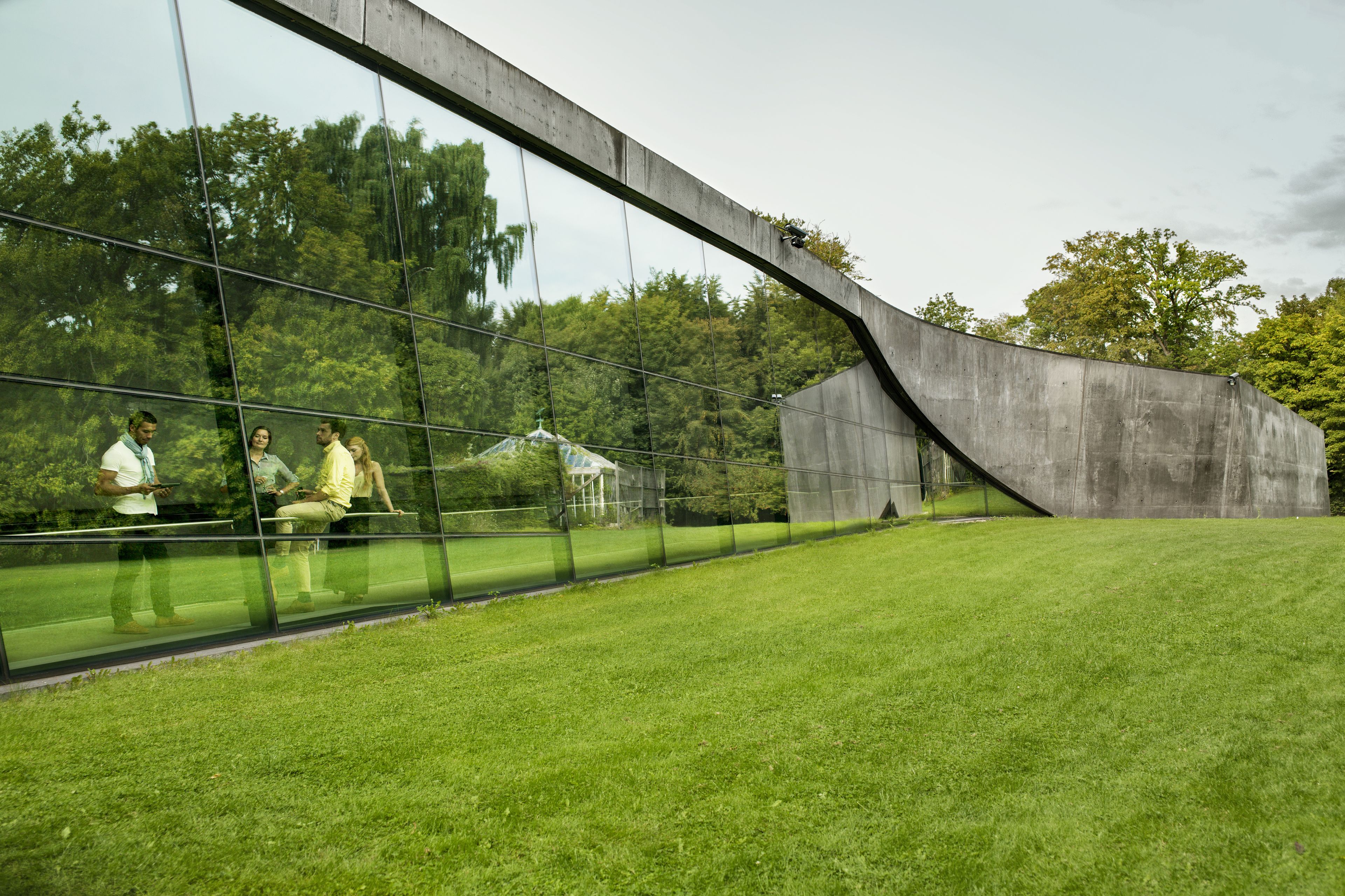 View of a building with large lawn outside and People inside a building visible through glass window