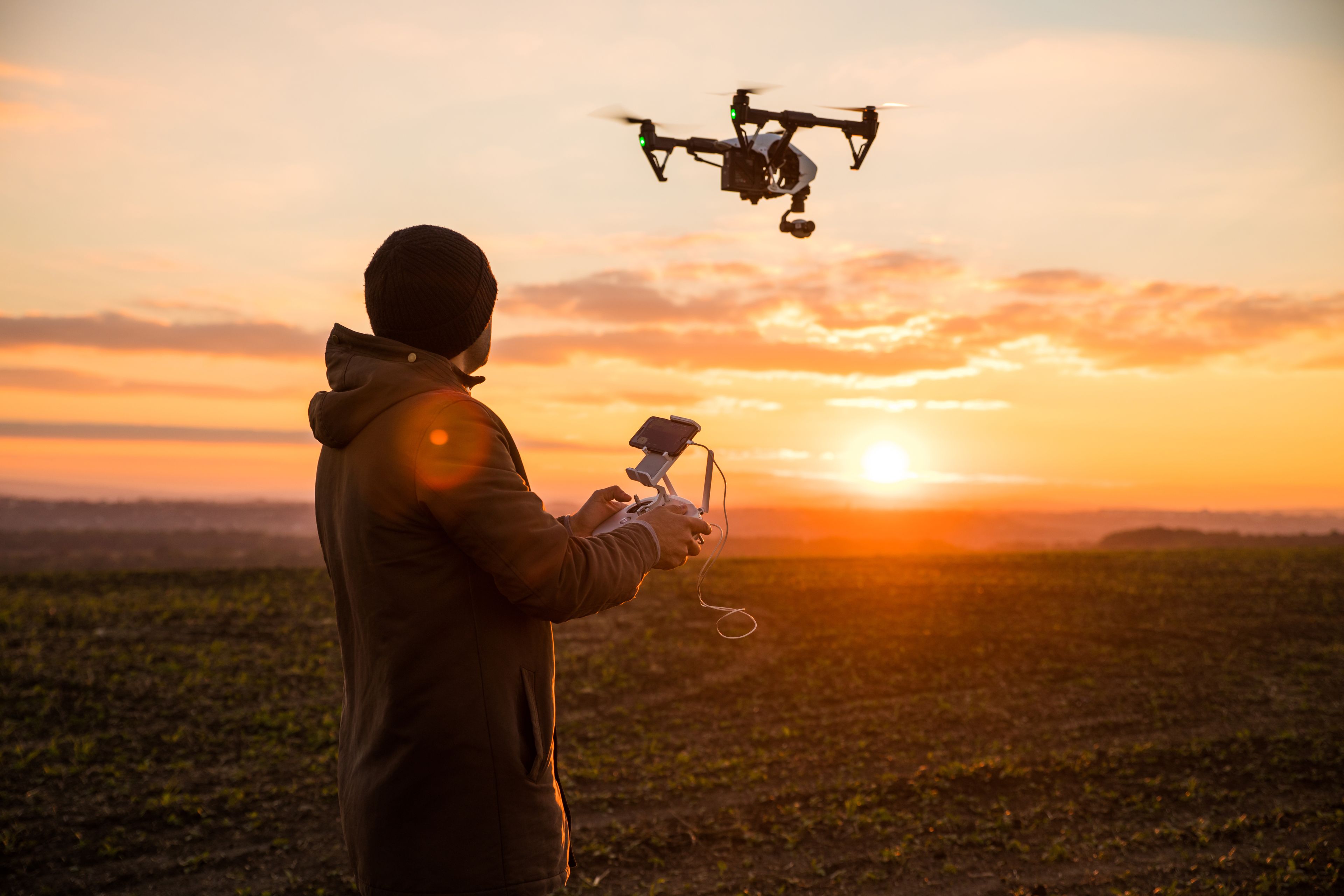 Man operating drone at sunset in field