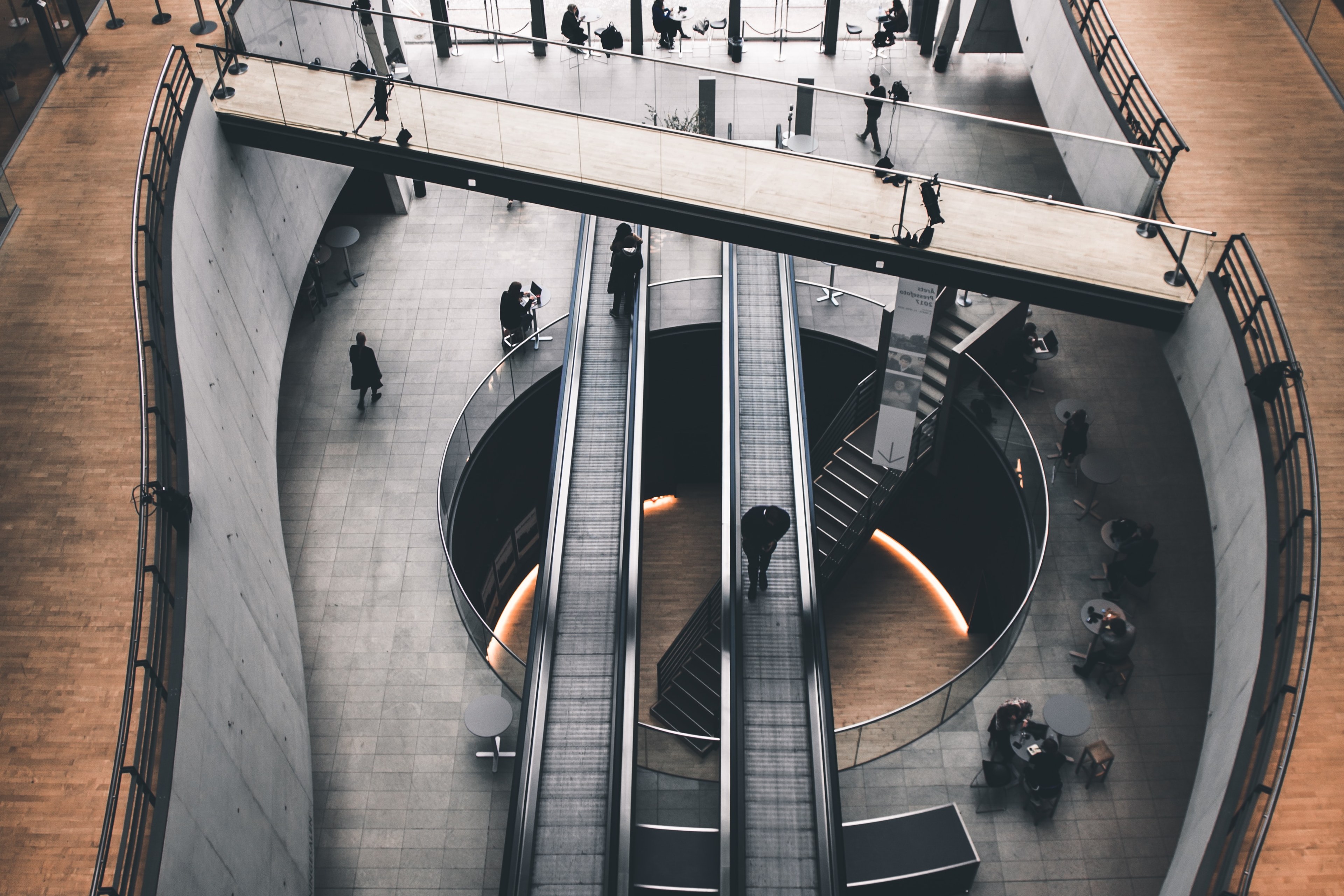 Ariel view of office with central stairs and escalators surrounded by people at desks