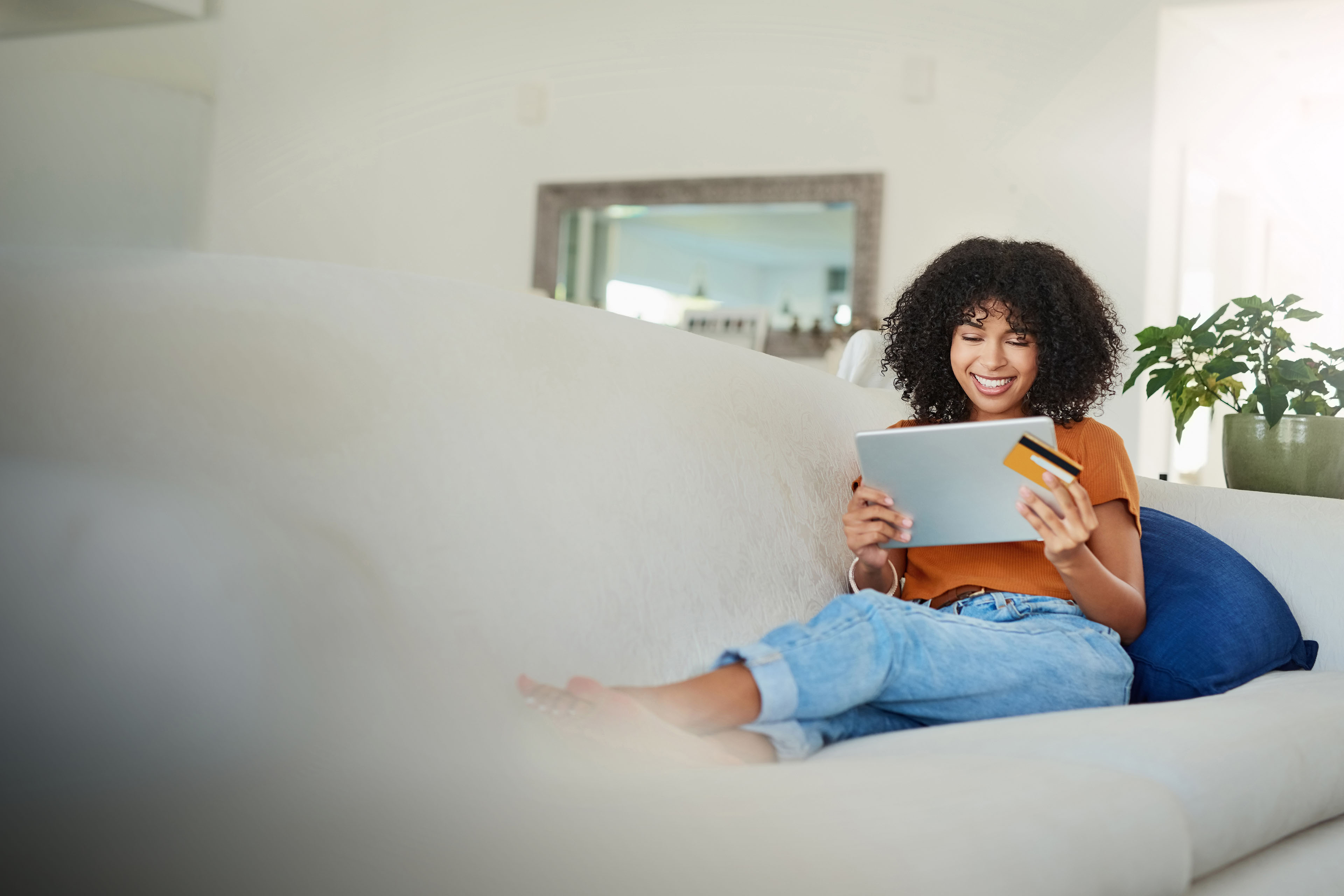 woman using a digital tablet and credit card on sofa at home