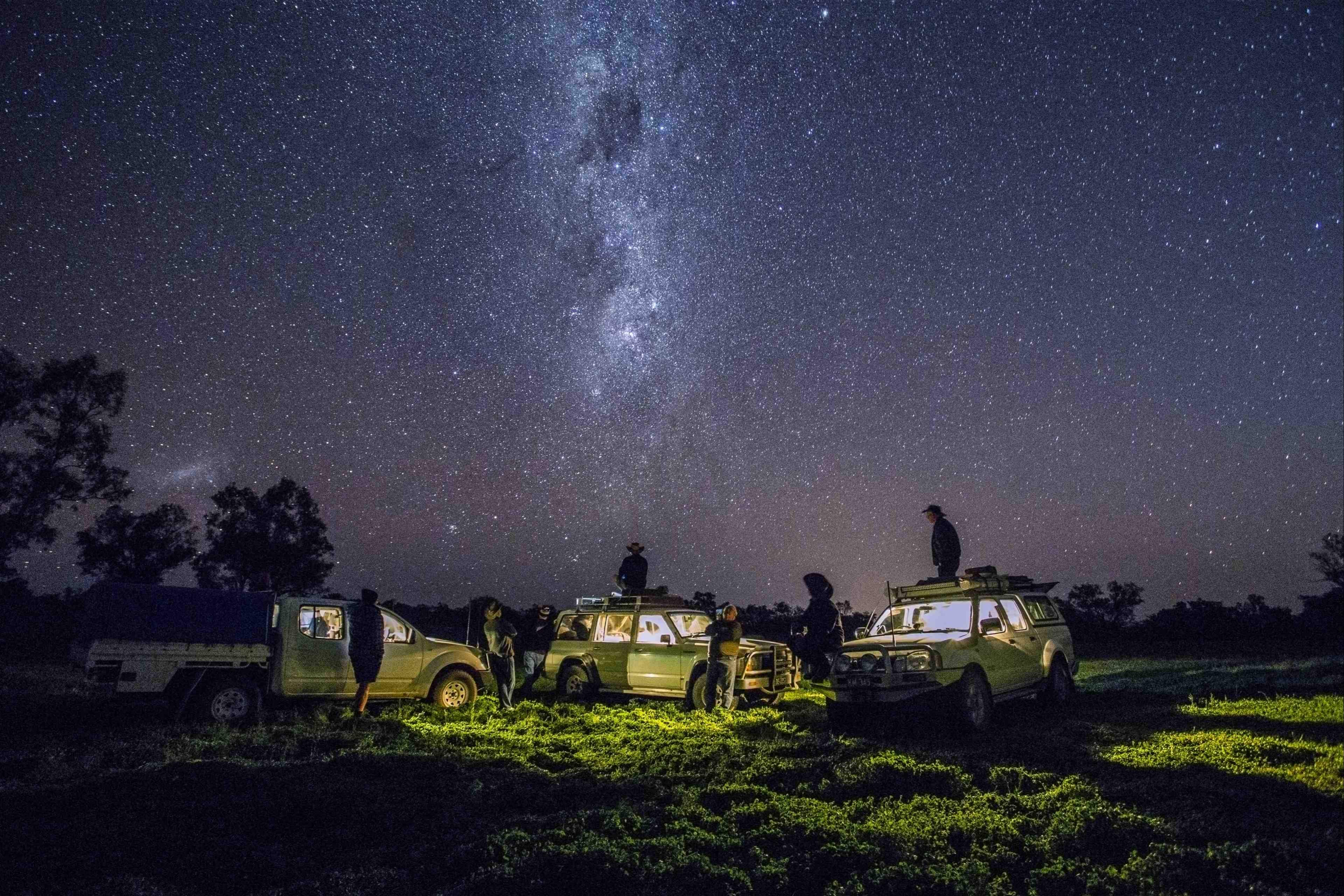 People standing on top of the cars and enjoying the view of stars in the sky