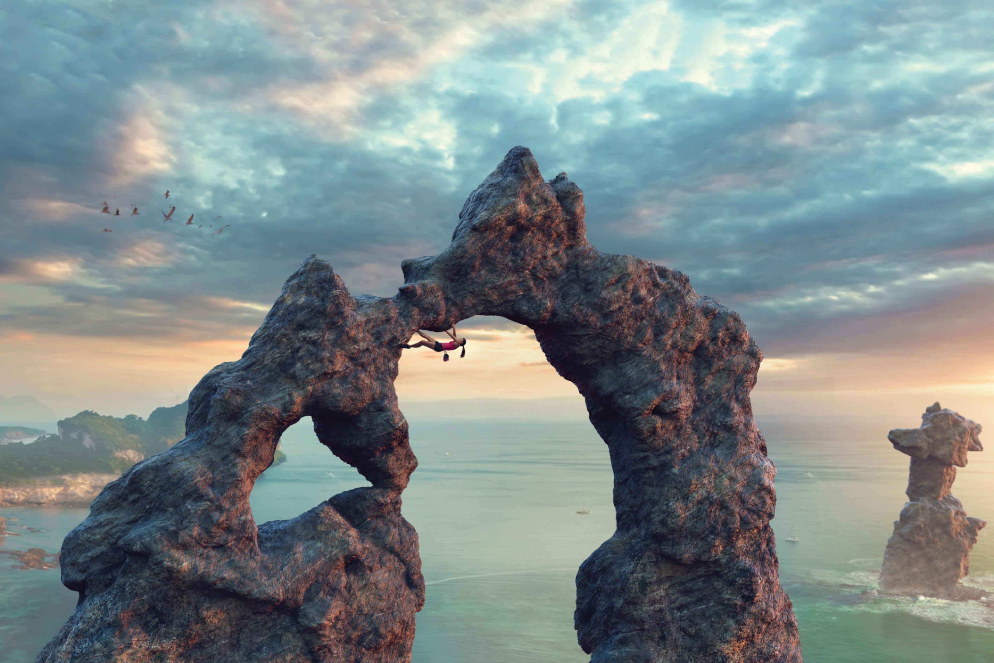 Free climber on rock arch near sea