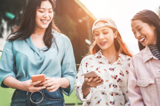 Three girls smiling and enjoying  together while two of them holding mobiles 