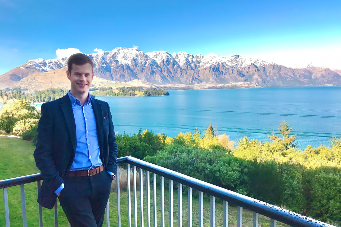 Person wearing a suit, standing against a background of mountains and ocean.