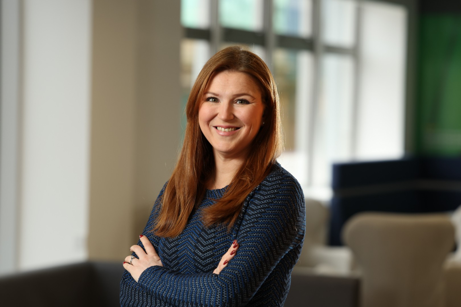 Photograph of a smiling woman with glass windows behind her.