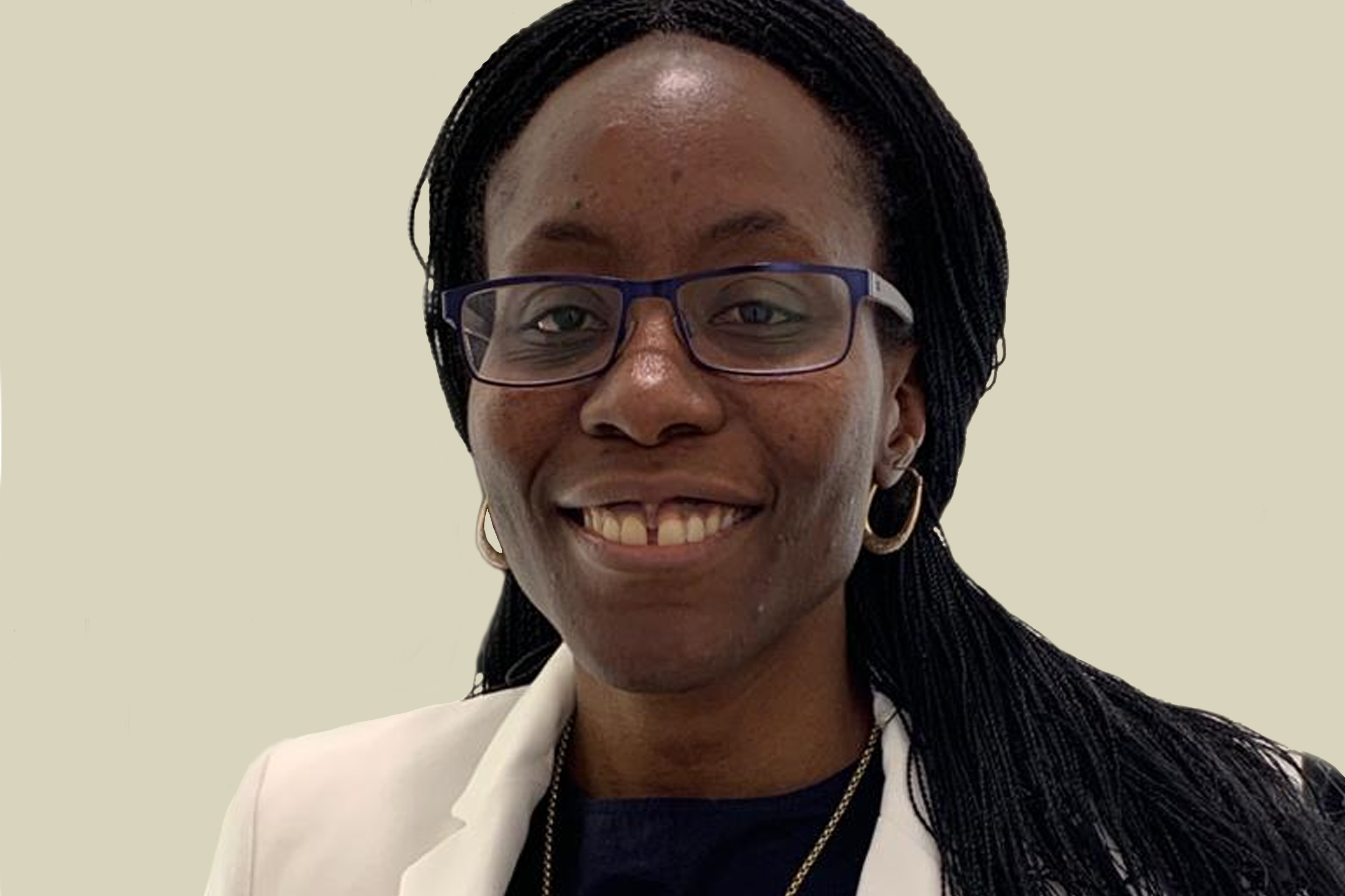 A woman wearing glasses, standing in front of a wall, and smiling.