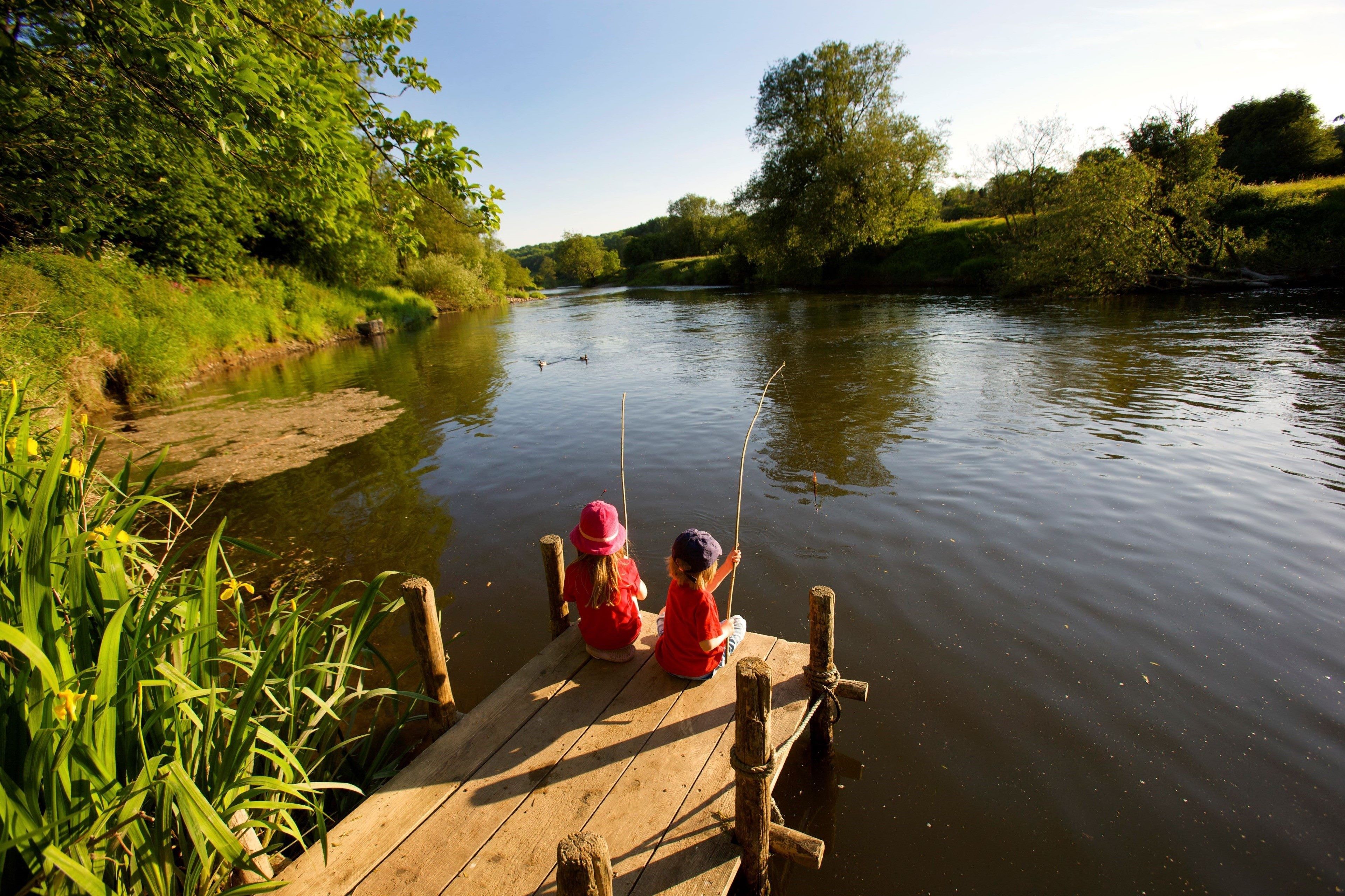 Photo of children sitting on a wooden platform fishing on a river