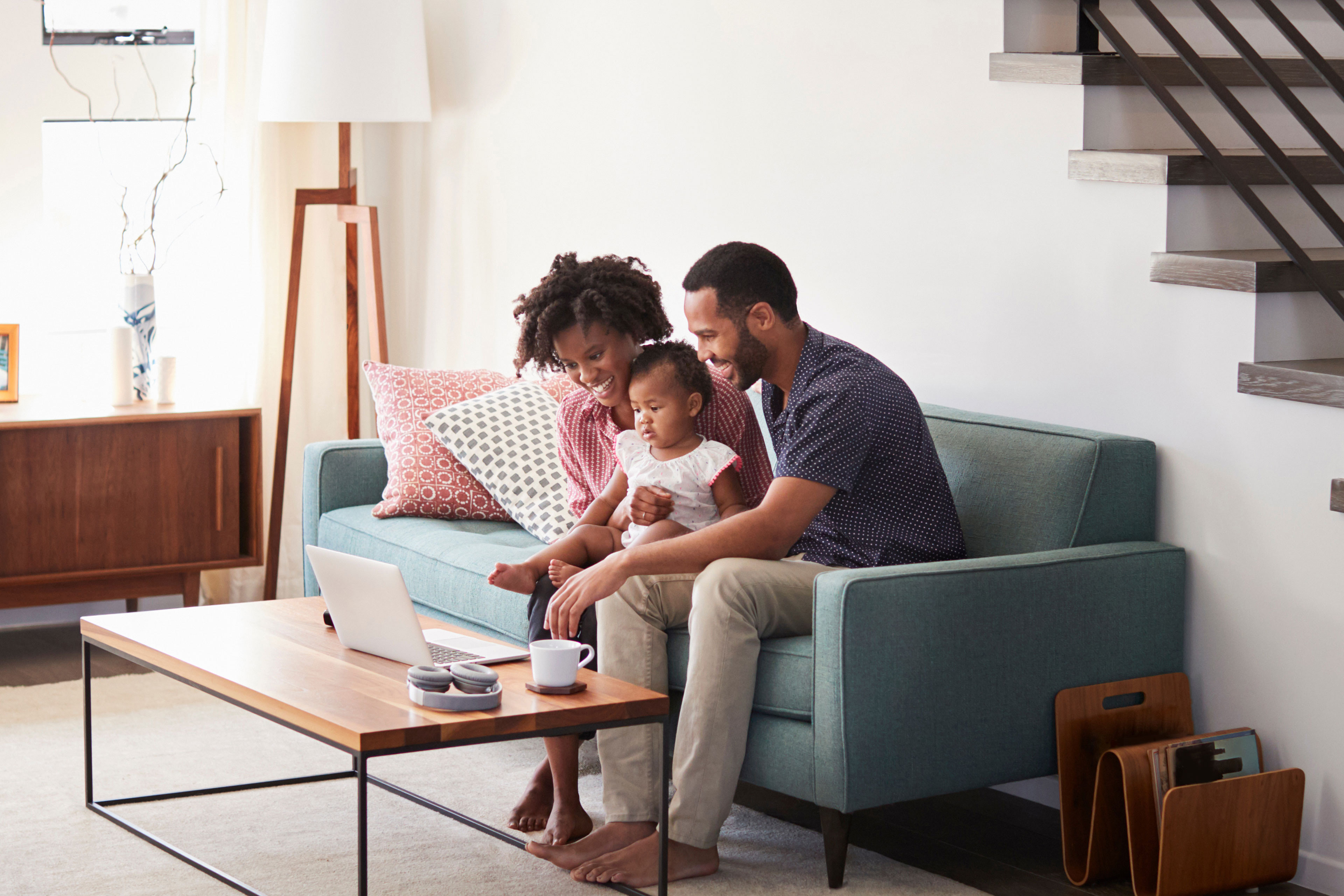 Family with baby daughter sitting on sofa at home looking at laptop computer