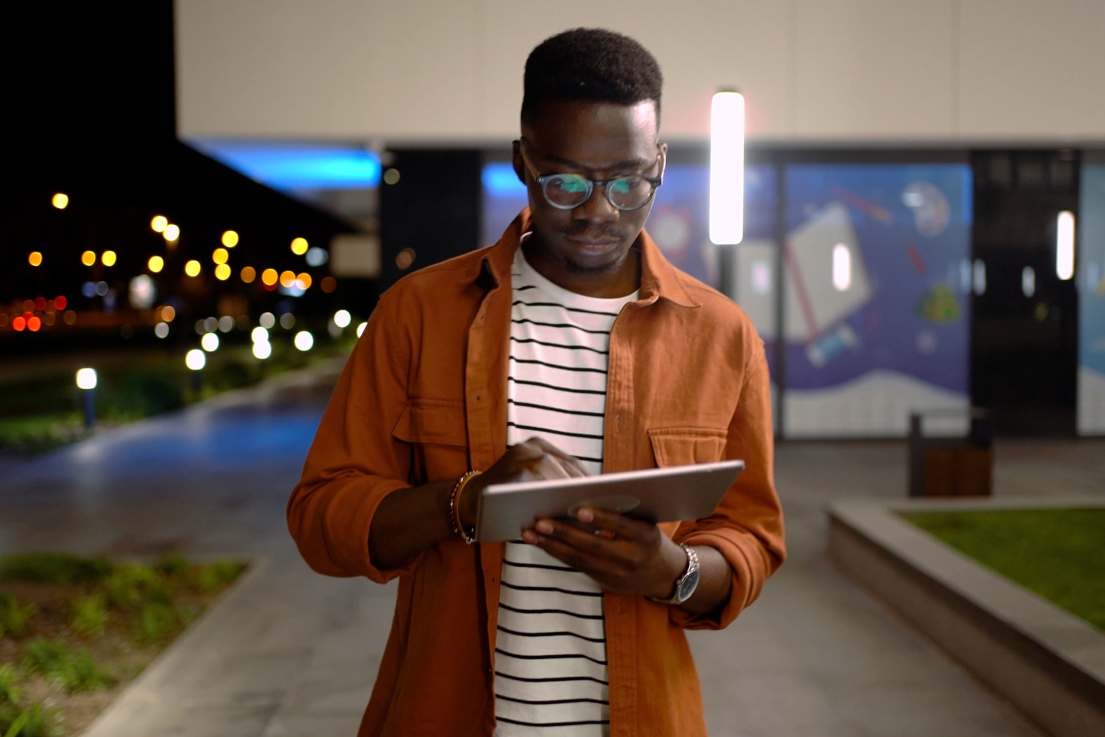 Man using his tablet while walking through the city at night