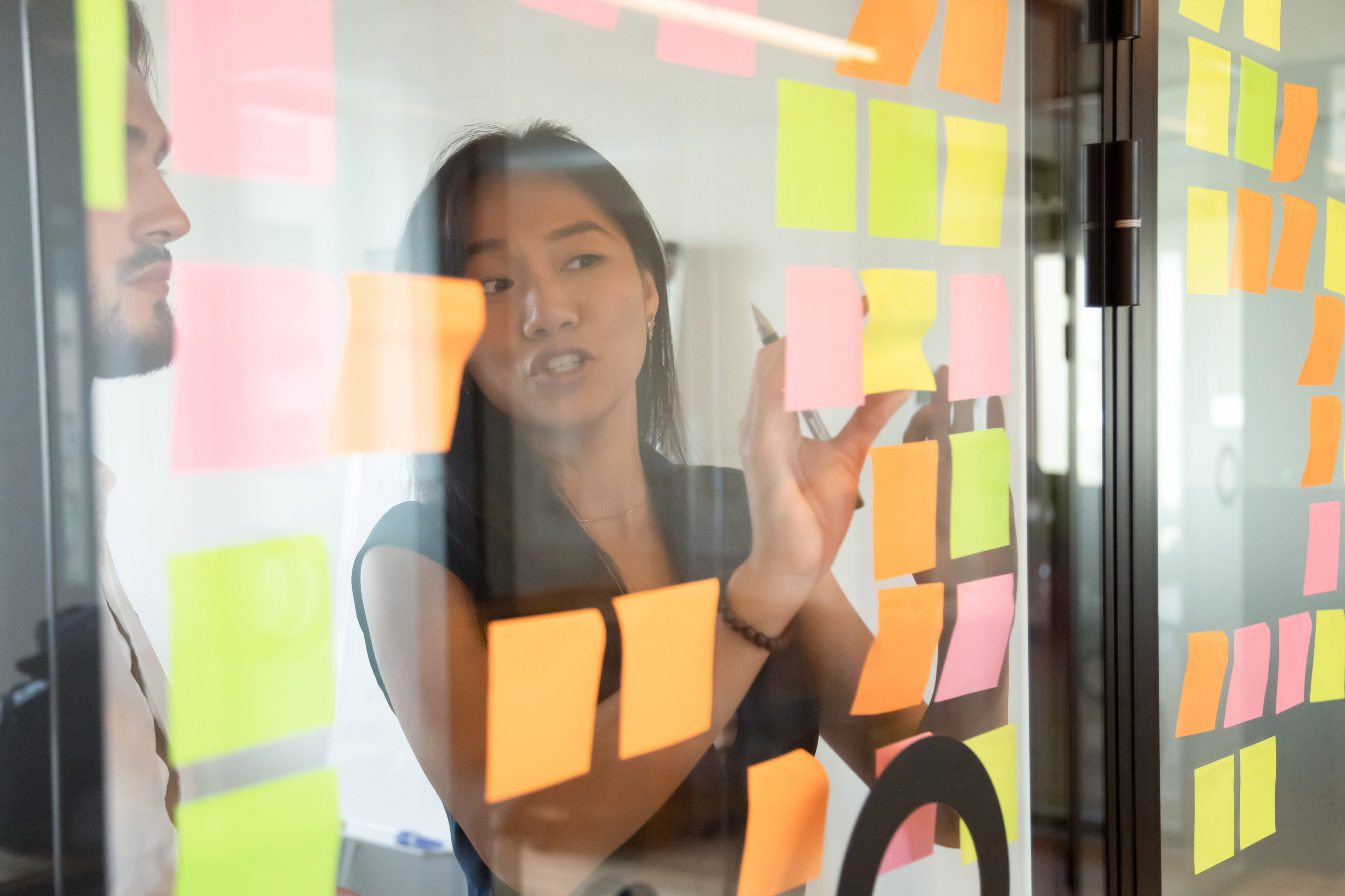 Colleagues working colourful post-it notes on glass