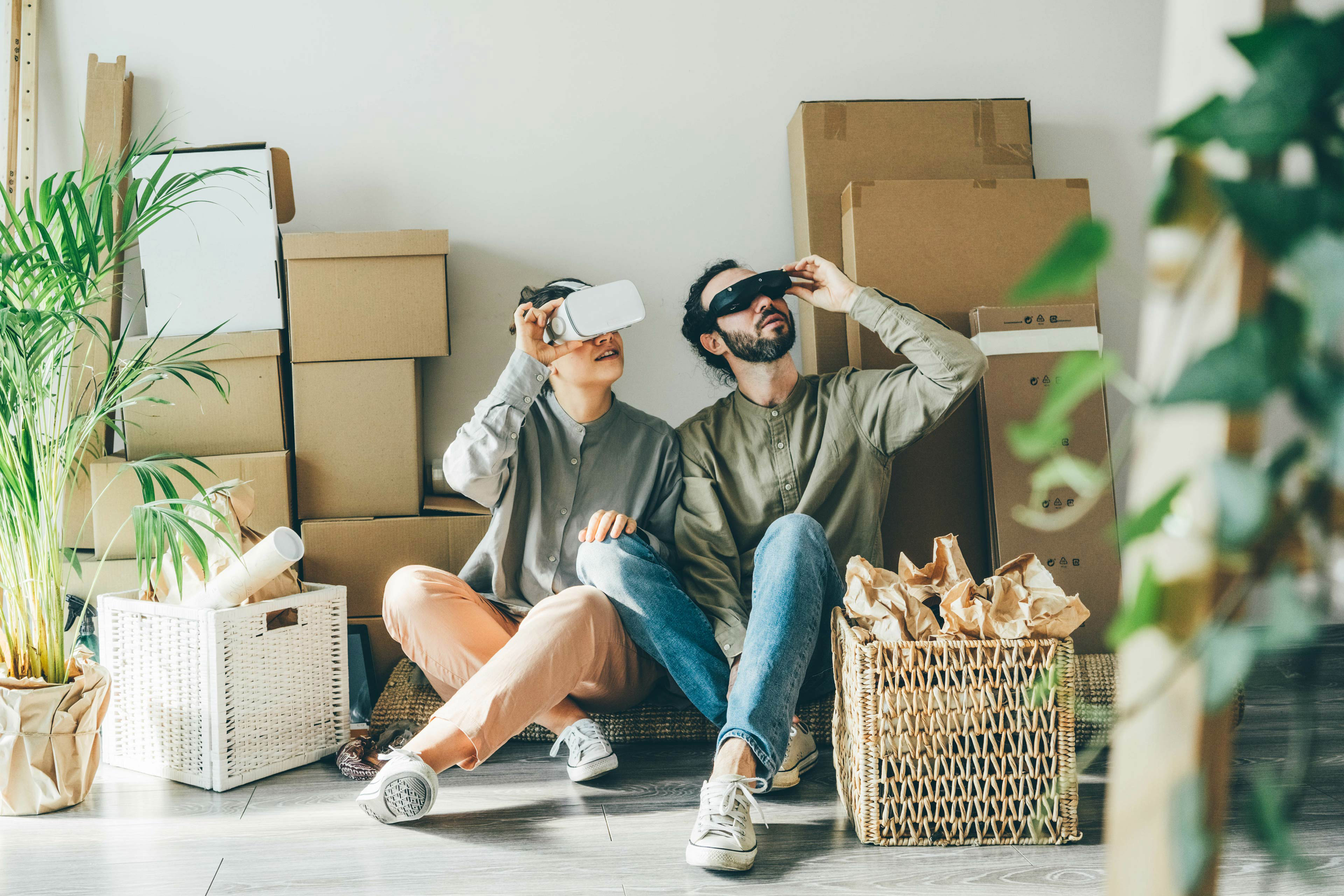 Happy young man and beautiful woman with modern virtual reality headsets sit on floor near numerous...