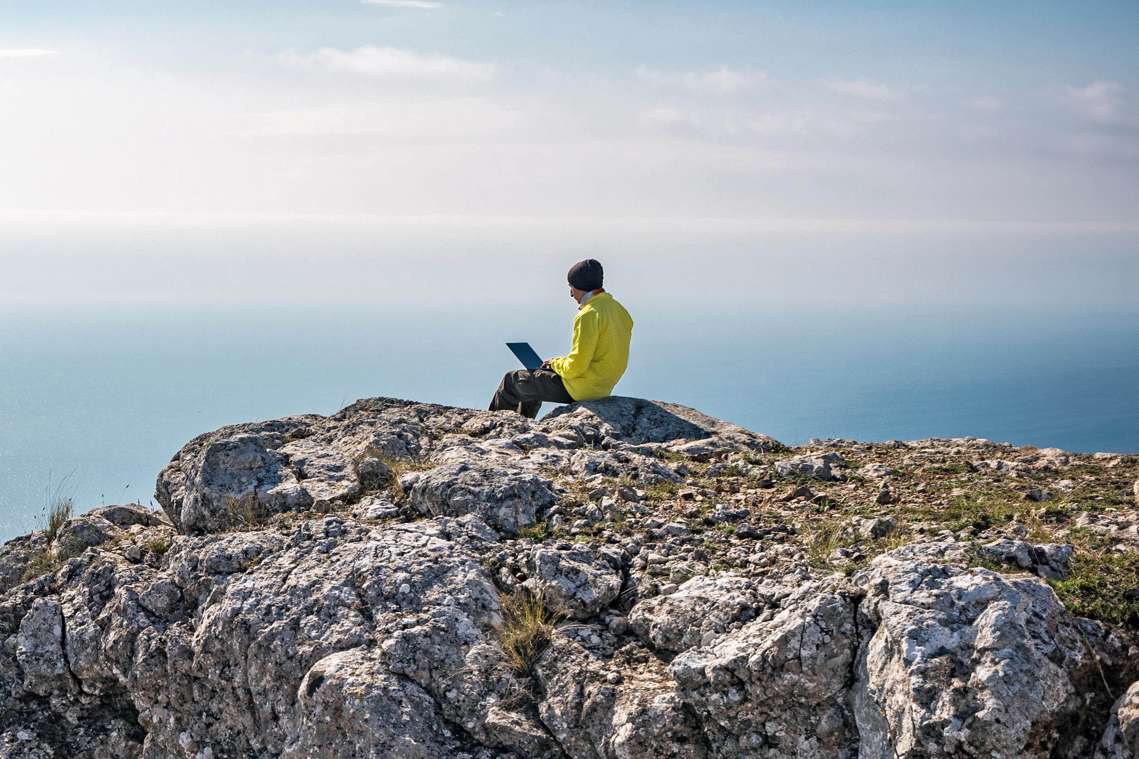 Freelancer typing on laptop on cliff at sea coast background